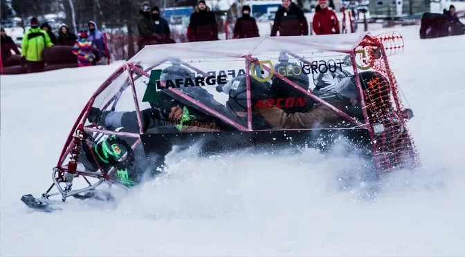 A snowmobile in a snow-covered field, with people watching in the background.