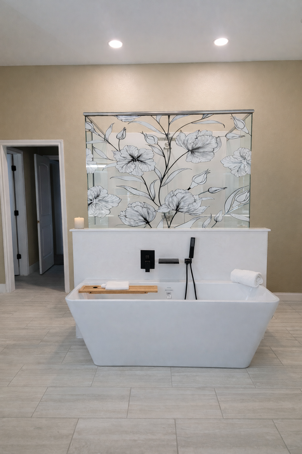 Modern bathroom with a white bathtub, a black faucet and showerhead, a rolled towel, a wooden bath tray, a small candle, and a decorative floral glass panel behind the tub.