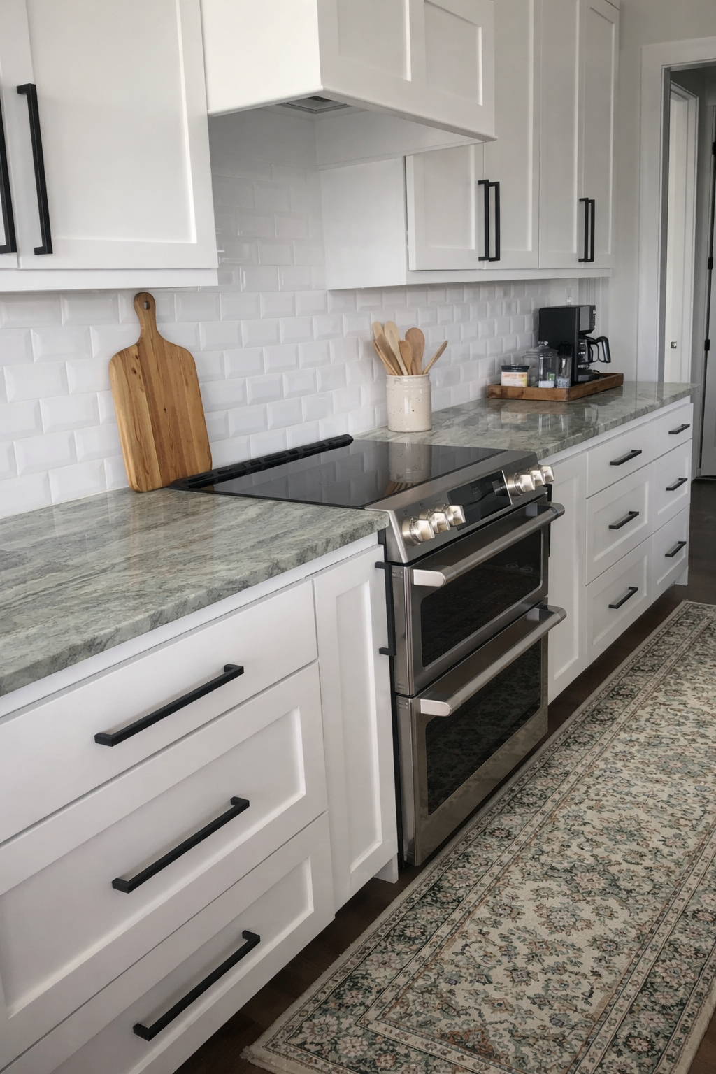 Kitchen with white cabinets, marble countertop, stainless steel oven, cutting board, utensils in a container, and coffee maker on a tray.