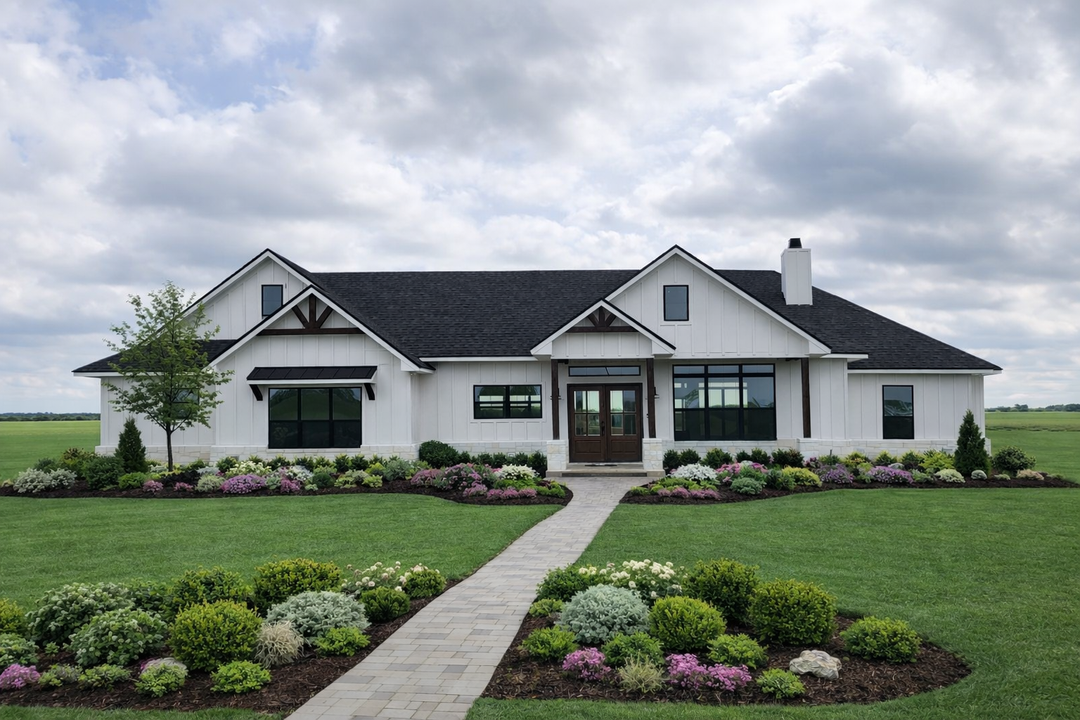A modern white house with black roof and large windows, surrounded by a well-manicured lawn and colorful flower beds