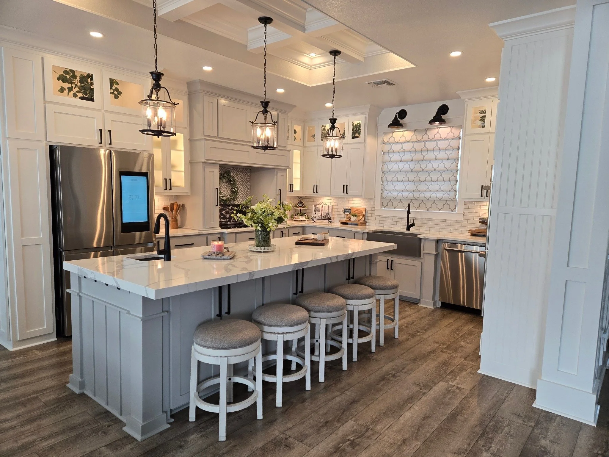 A modern kitchen with white cabinets, a large kitchen island with seating, stainless steel appliances, and pendant lighting.