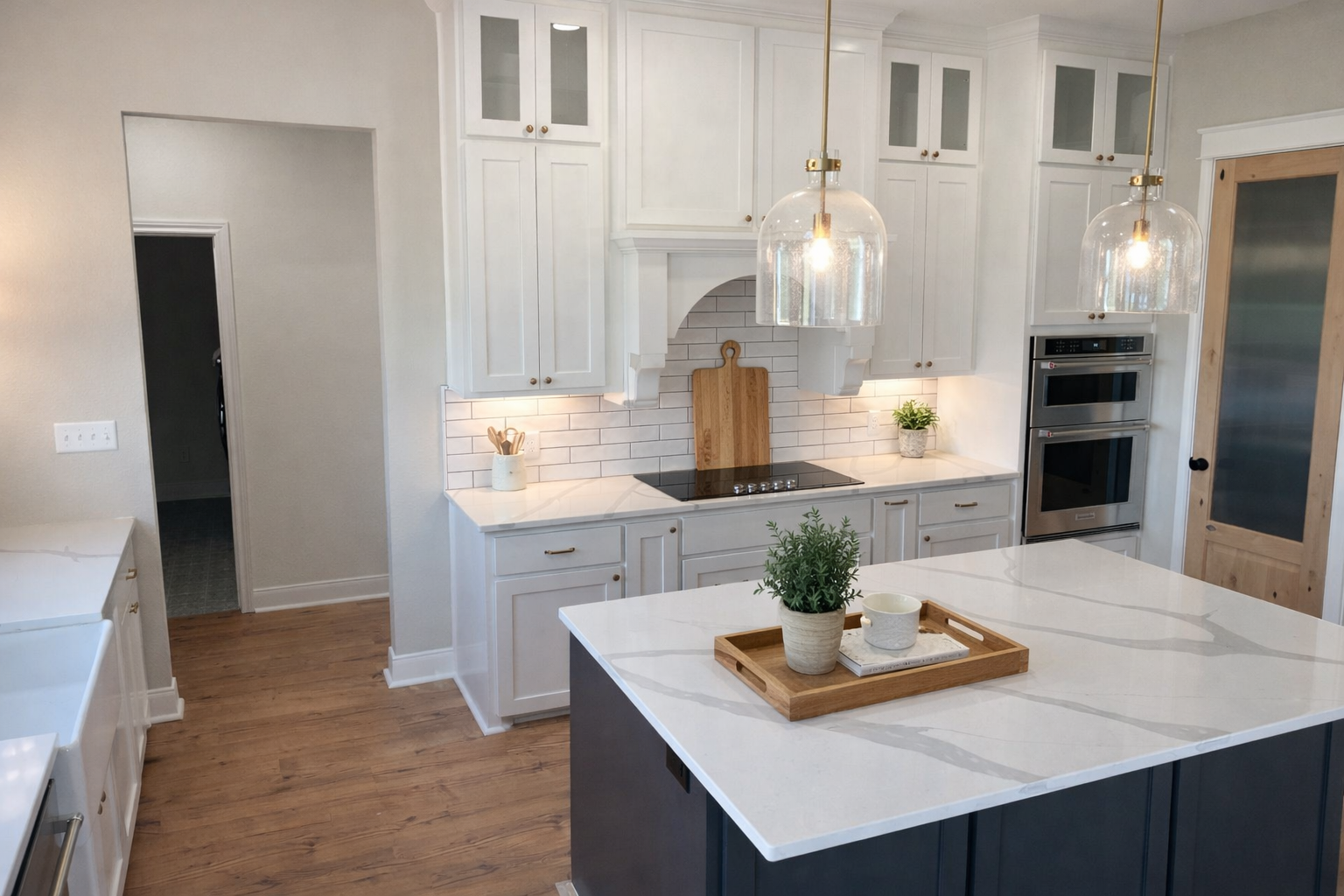 Modern kitchen with white cabinets, a large island with a white marble countertop, pendant lights, and stainless steel double ovens.