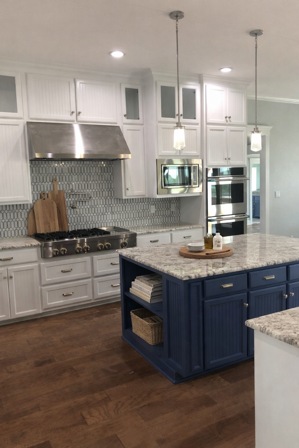 Modern kitchen with white cabinets, stainless steel appliances, a blue island with a marble countertop, and wooden flooring.