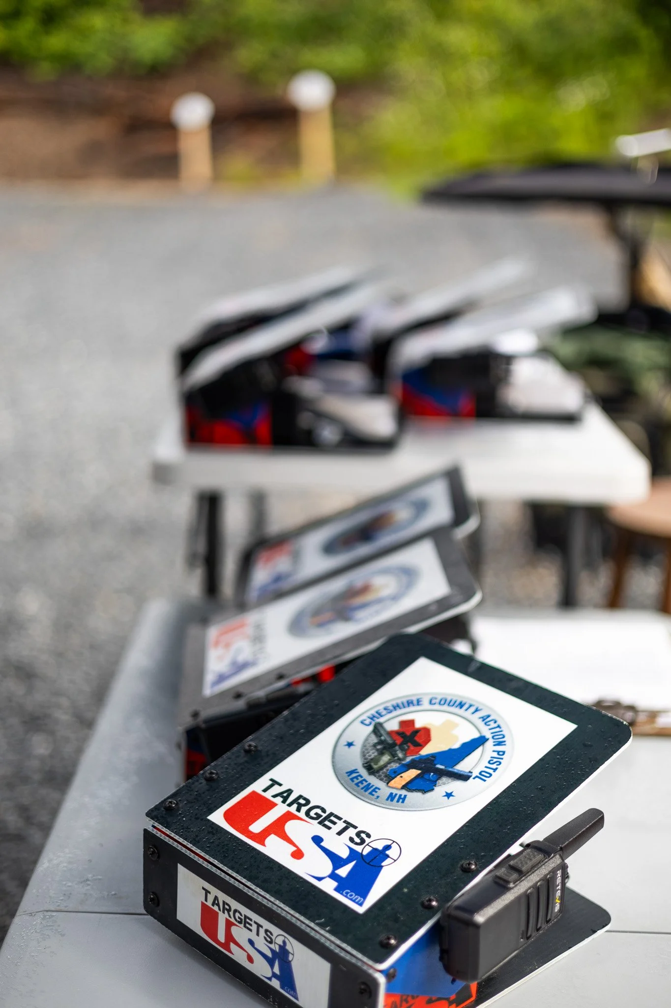 Close-up of Black Target USA shooting target boxes with an emblem of Cheshire County Action Pistol, Keene, NH, placed on a gray surface.