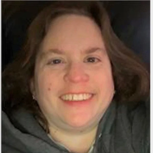Close-up of a smiling woman with shoulder-length brown hair, wearing a dark gray hoodie.