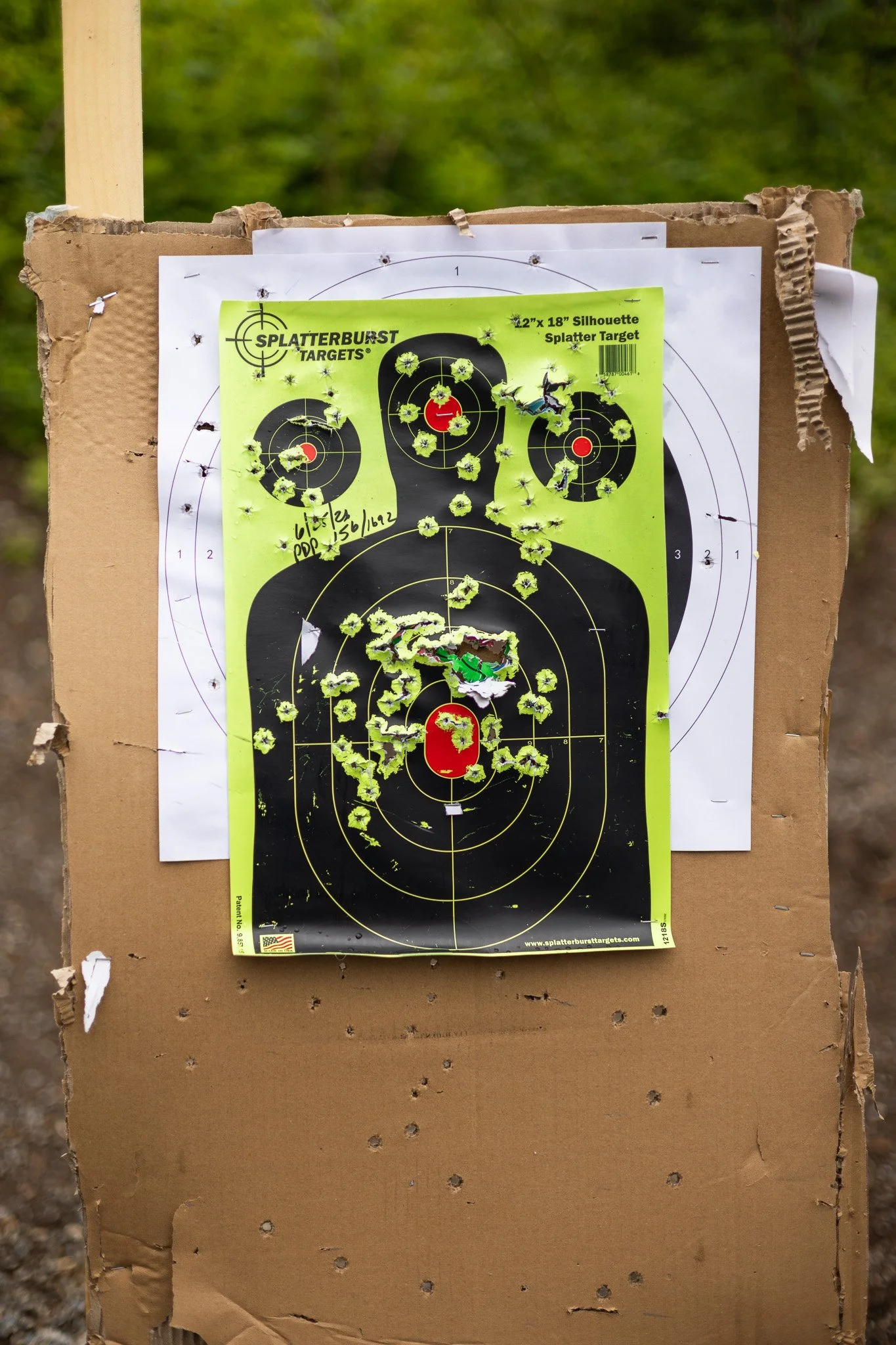 A shooting target on an outdoor cardboard stand, punctured with numerous bullet holes, with a black and yellow round target on a yellow paper background.