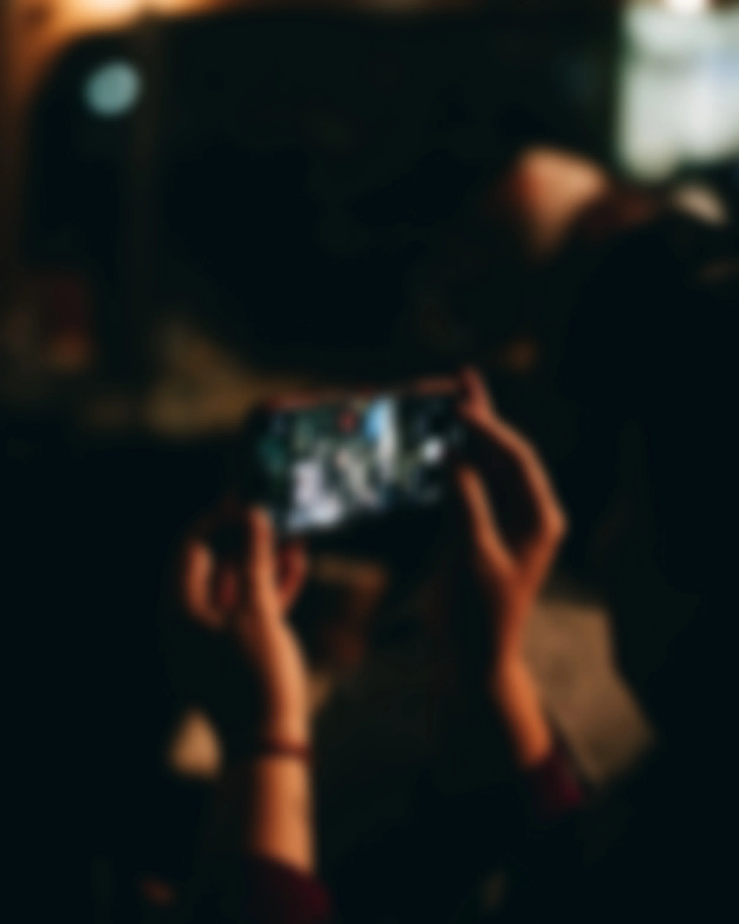 Person holding a smartphone, appears to be taking a photo or video, in a dimly lit room.