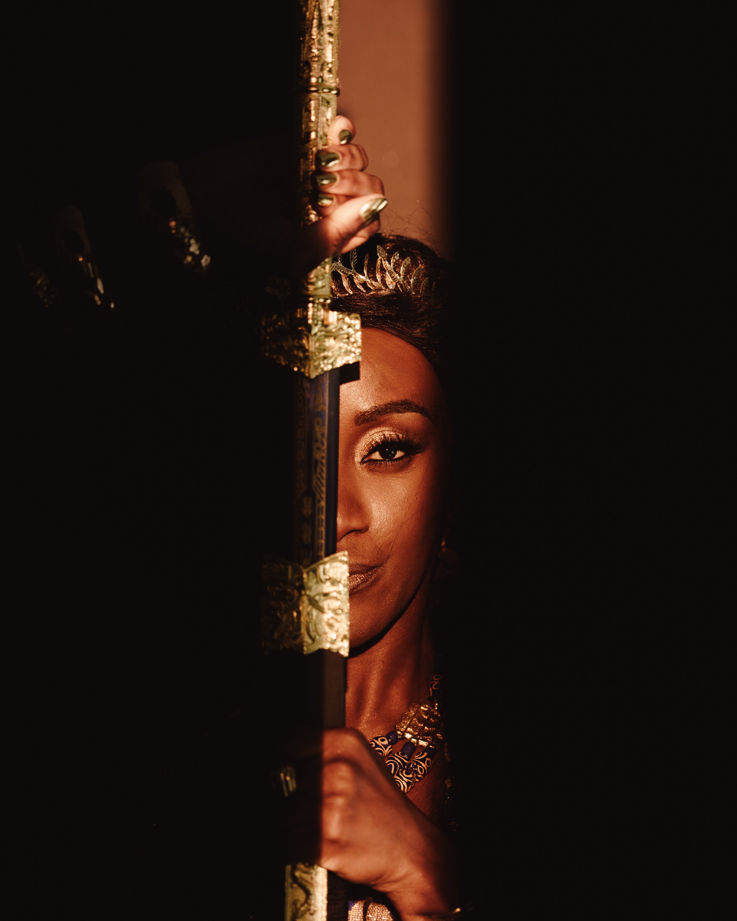 A woman peeks through a narrow opening, revealing half of her face, adorned with golden jewelry and makeup.