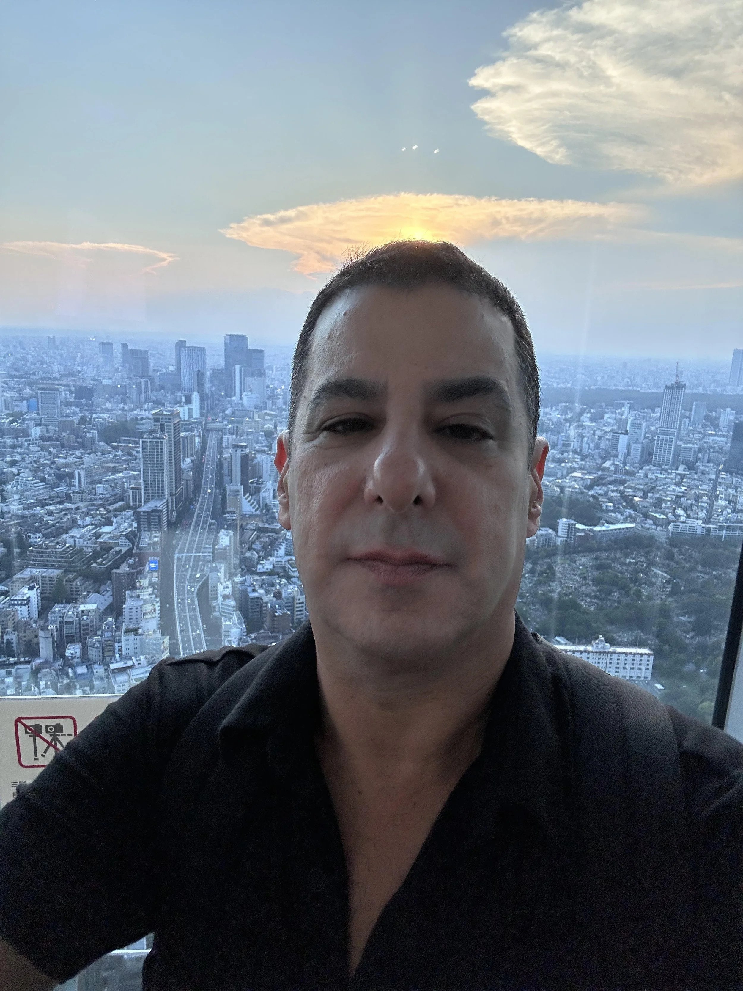 Selfie of a man taking a photo in a tall building with a city skyline and sunset in the background.