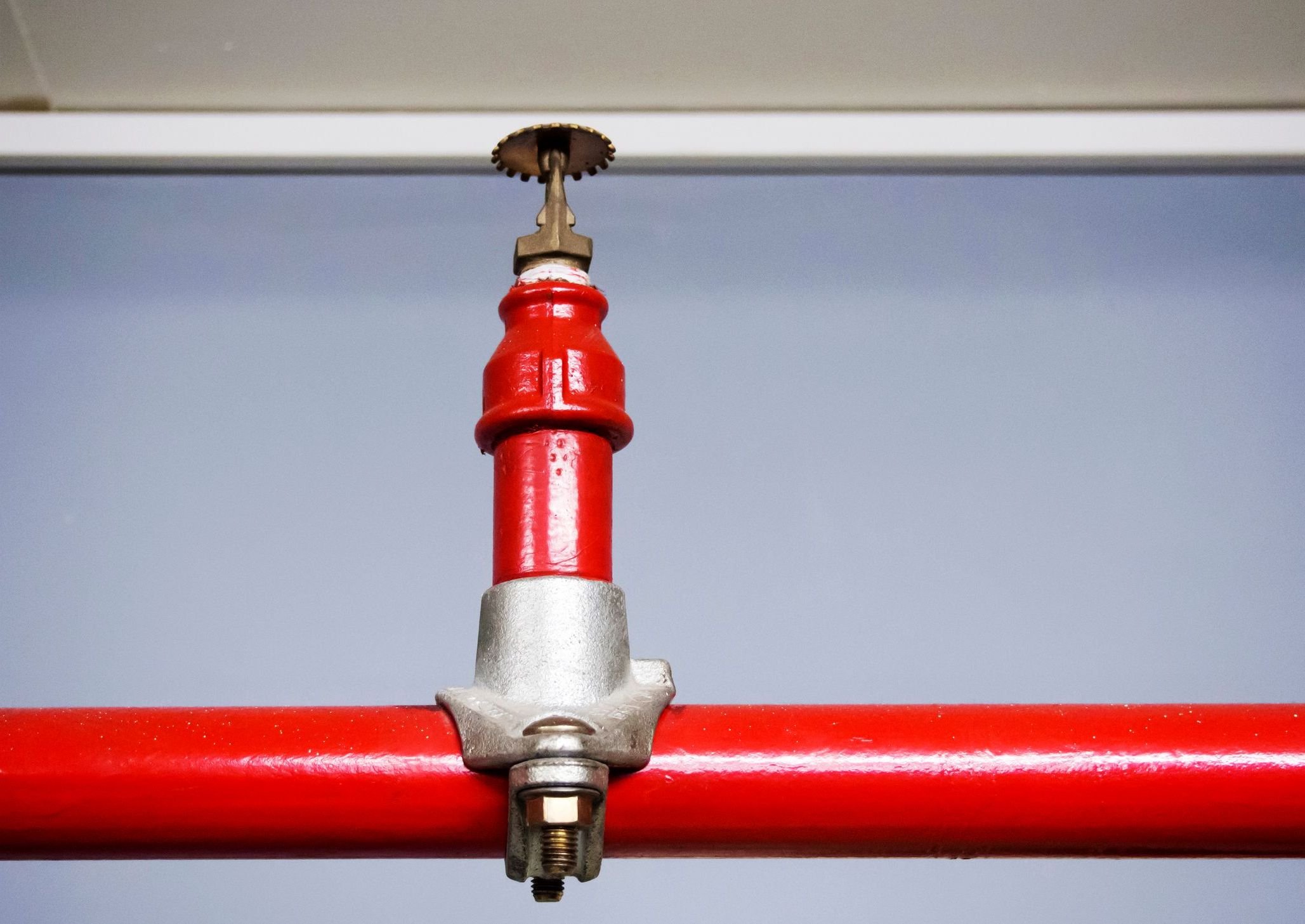A close-up of a red-painted metal pipe with a valve assembly against a light blue sky background.