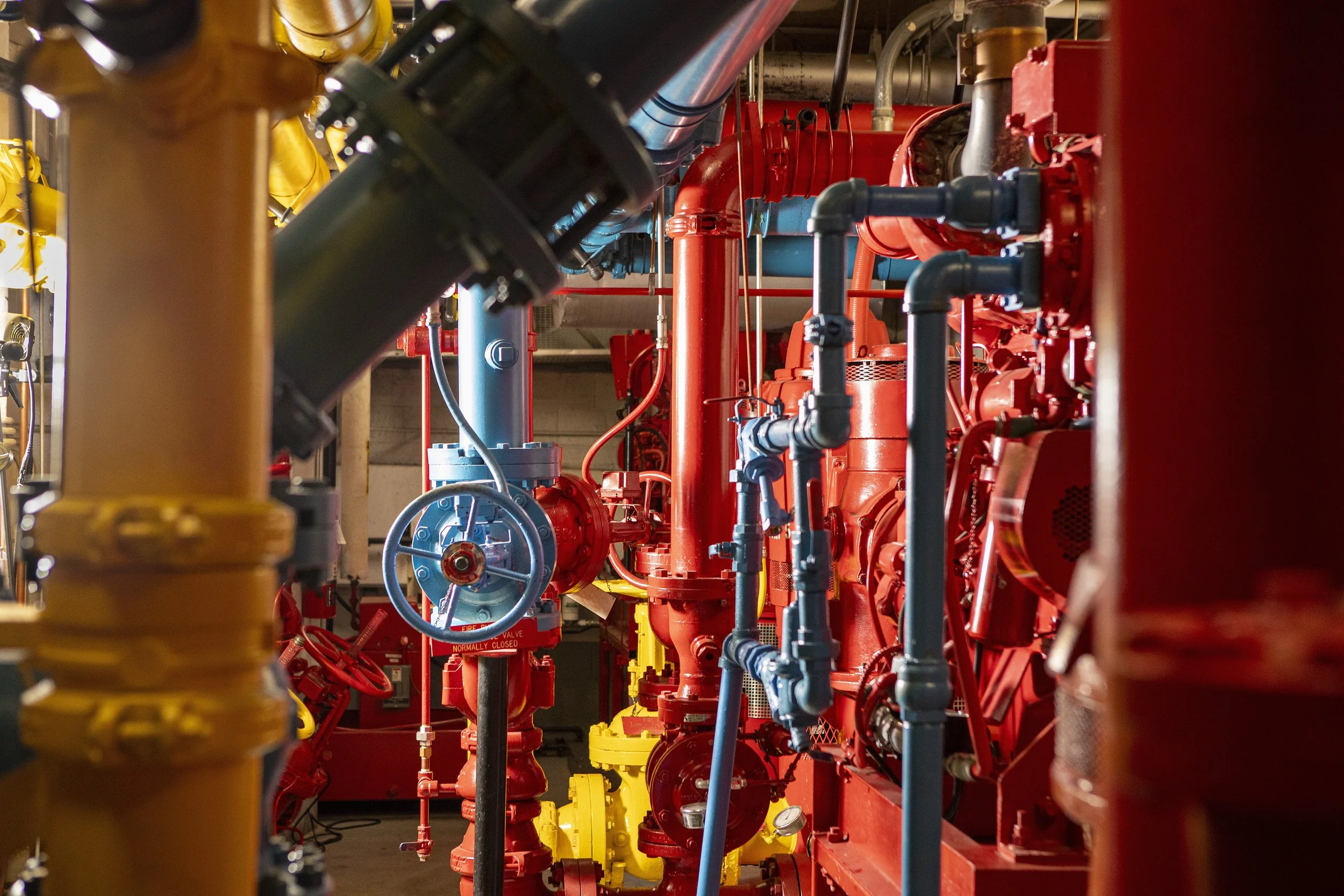 Industrial machinery with interconnected colored pipes, valves, and equipment in a mechanical room.
