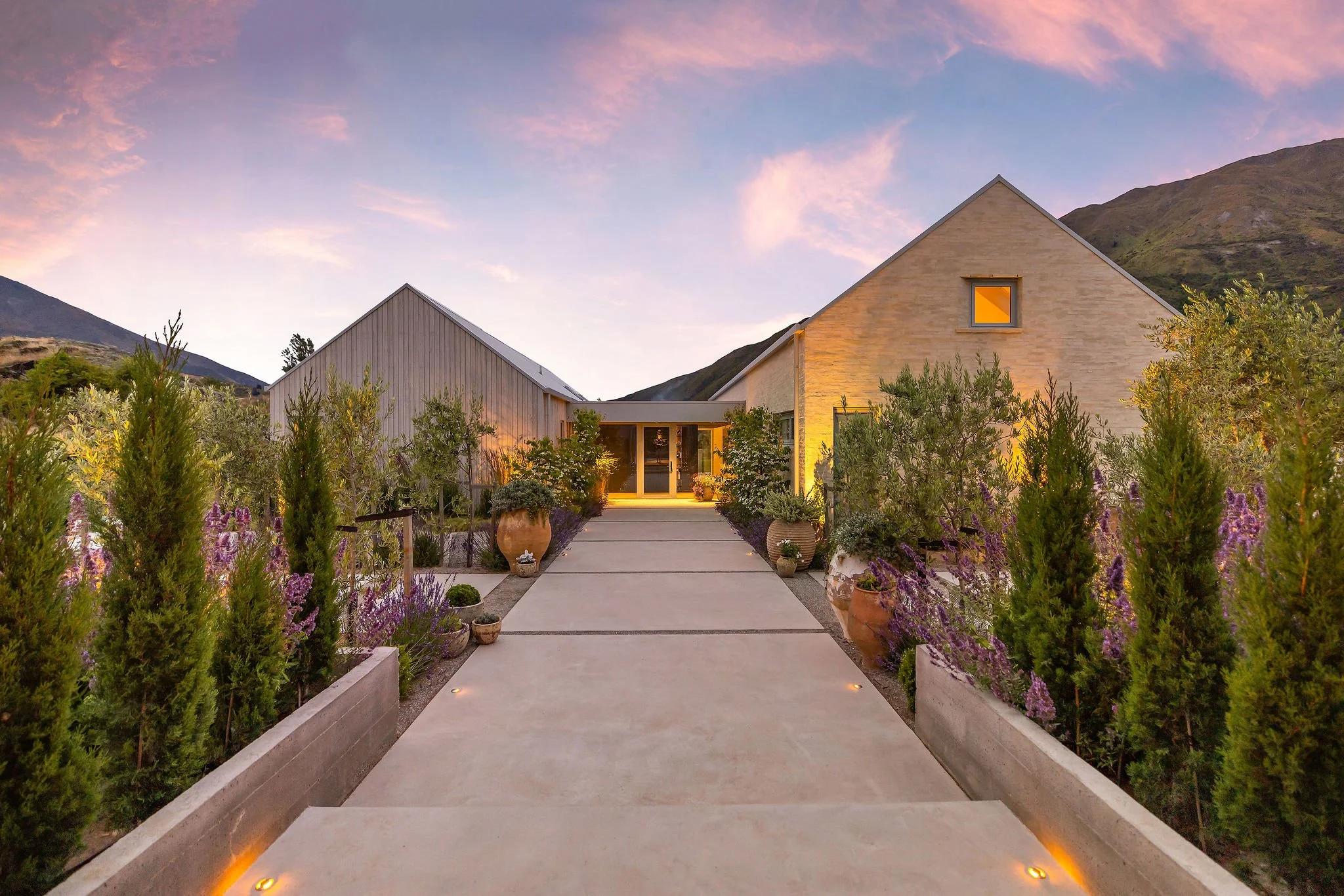Looking towards the home with feature concrete work and tree lined pathways during sunset at Peregine Ridge, a Gibbston Valley home built by Diemarco Builders Queenstown.