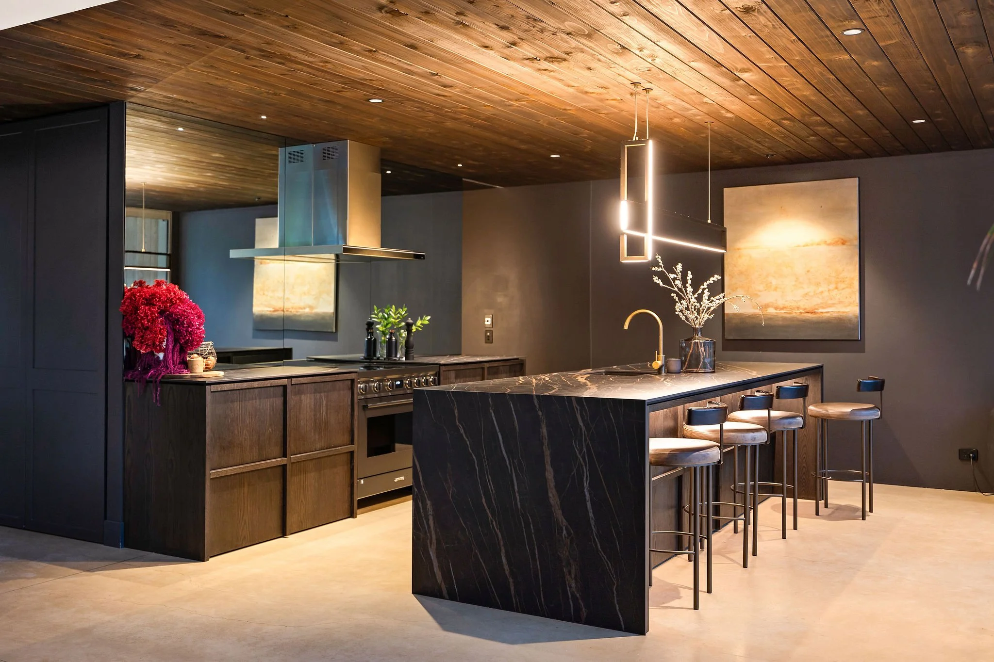 A dark yet luxurious kitchen with custom benchtops and feature lighting at Peregine Ridge, a Gibbston Valley home built by Diemarco Builders Queenstown.