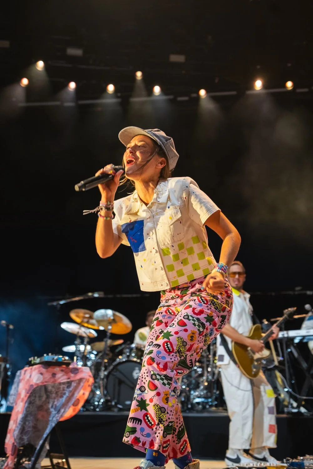 Singer in colorful outfit performing on stage with band and musician playing guitar in the background, under stage lights. Professional Photographer in Kalispell, Montana in the Flathead Valley