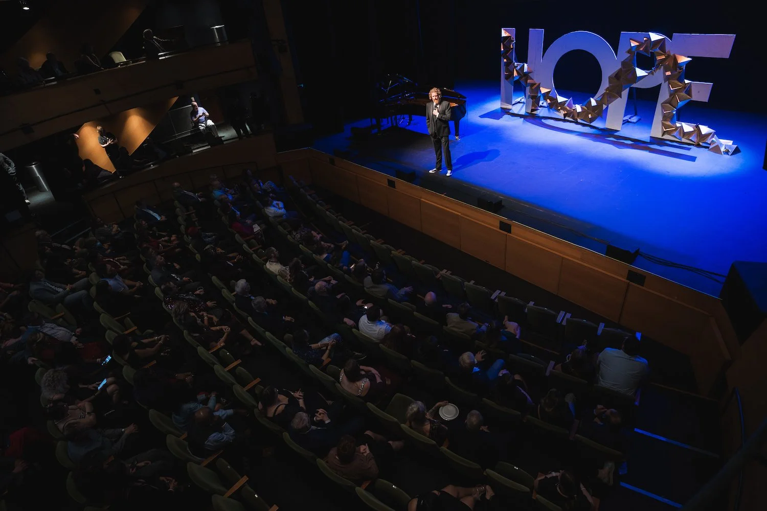 Person on stage with a large 'HOPE' sign addressing an audience in a theater. Professional Event Photographer in Kalispell, Montana in the Flathead Valley.