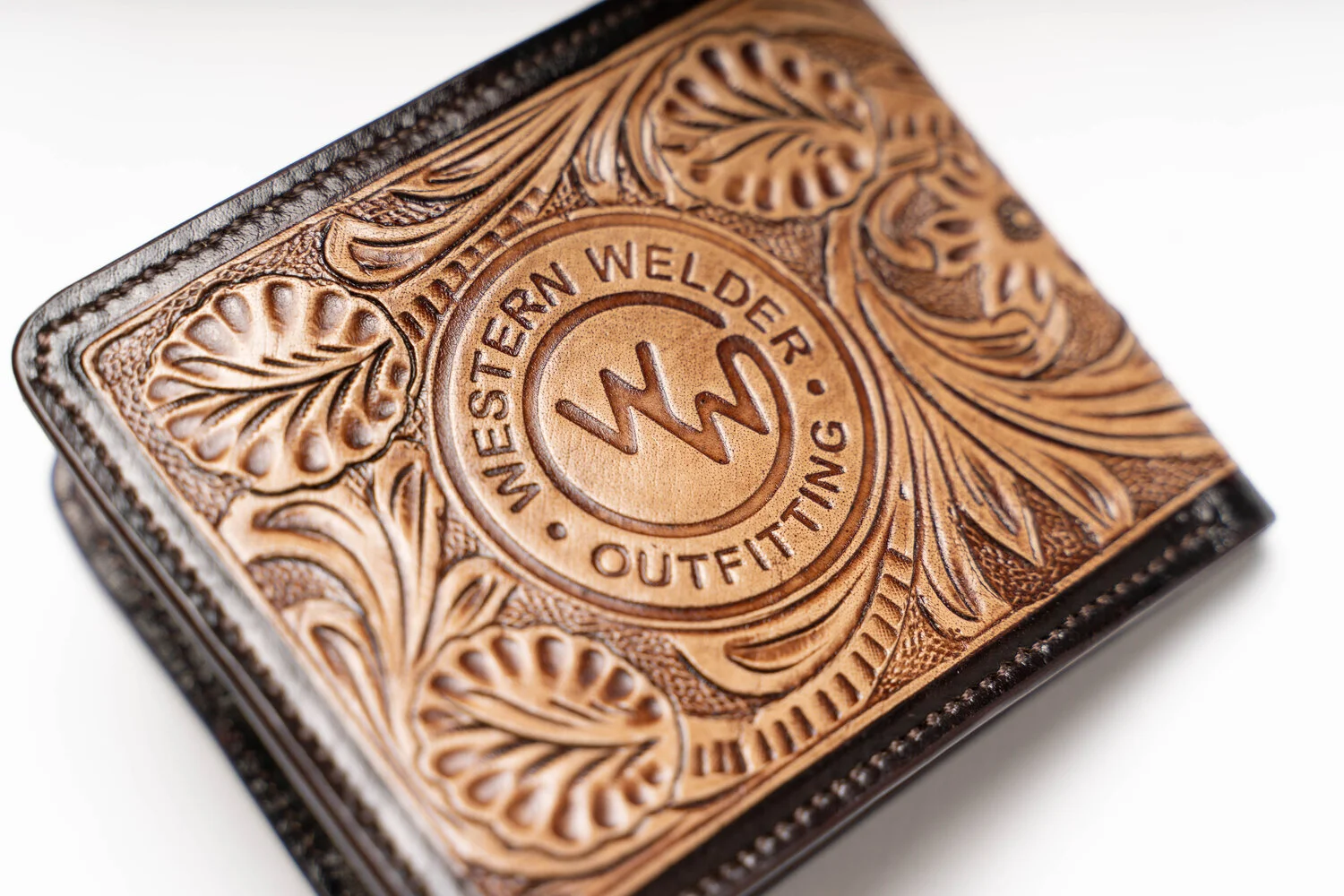 Close-up of a leather wallet with intricate floral engraving and "Western Welder Outfitting" logo. Product Photographer in Kalispell, Montana in the Flathead Valley