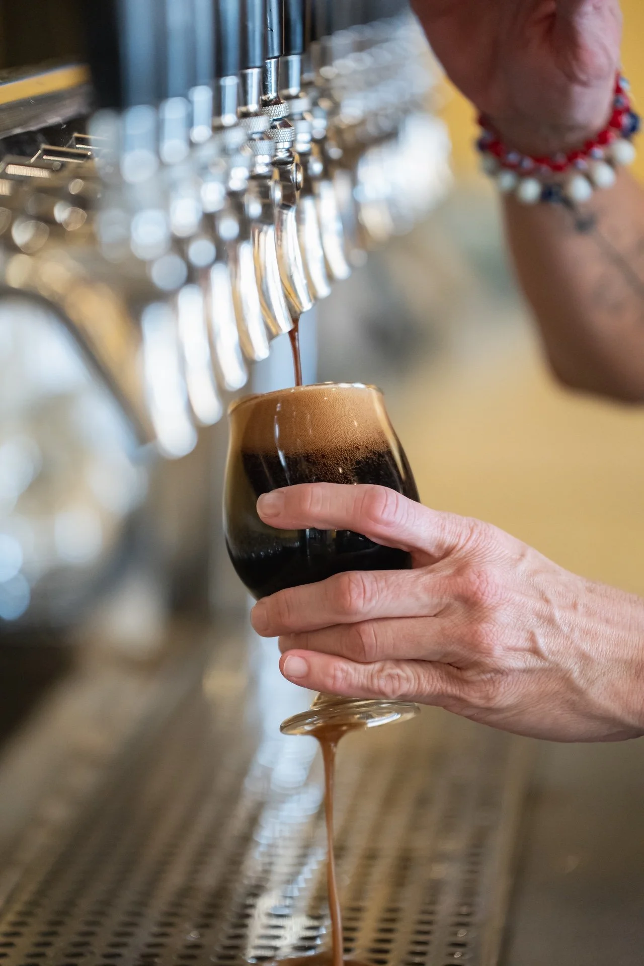 A person is pouring dark beer from a tap into a glass with a frothy head at a bar or brewery. Food Photographer in Kalispell, Montana in the Flathead Valley