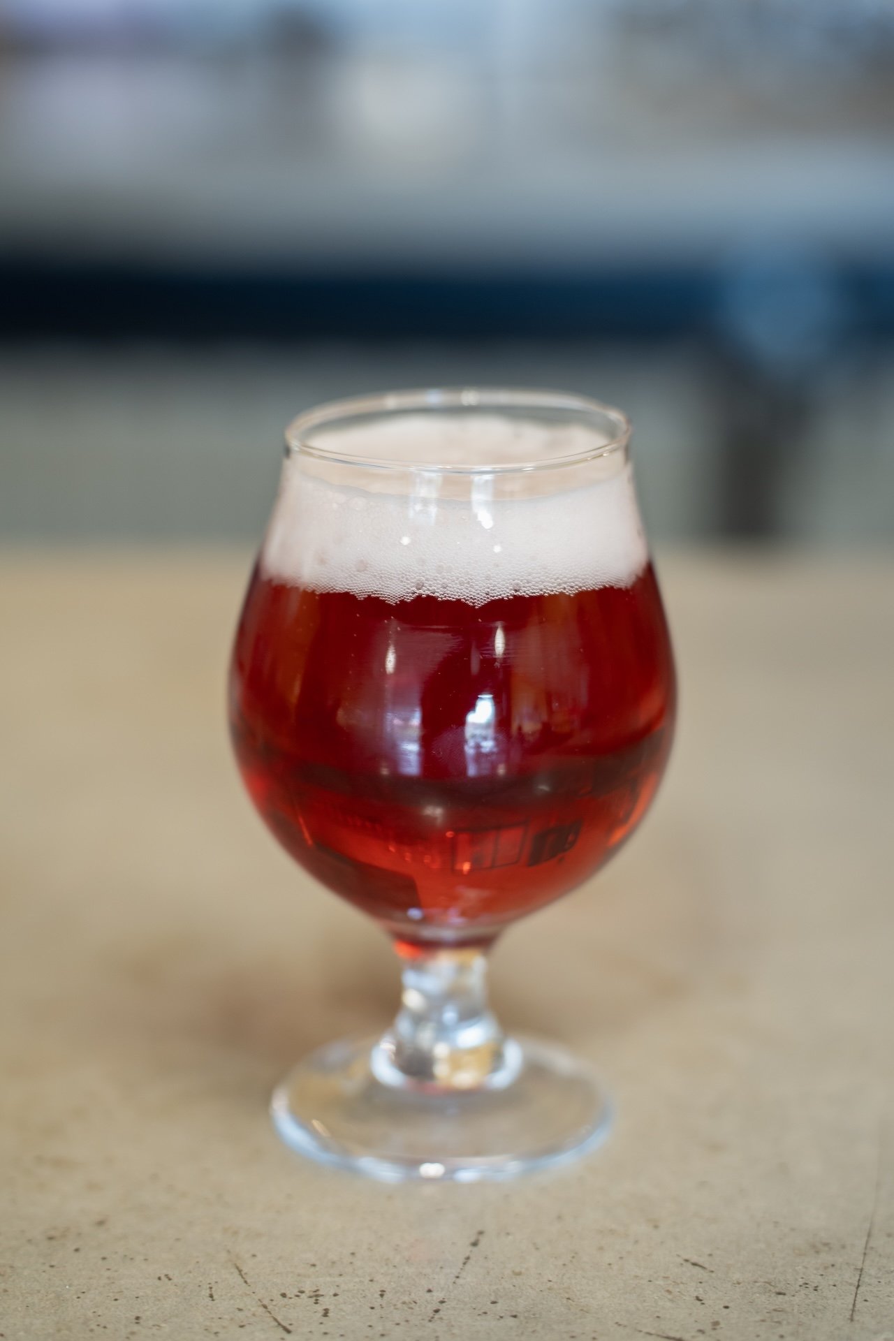 A glass of red beer with a foamy head on top, placed on a light-colored surface. Food Photographer in Kalispell, Montana in the Flathead Valley