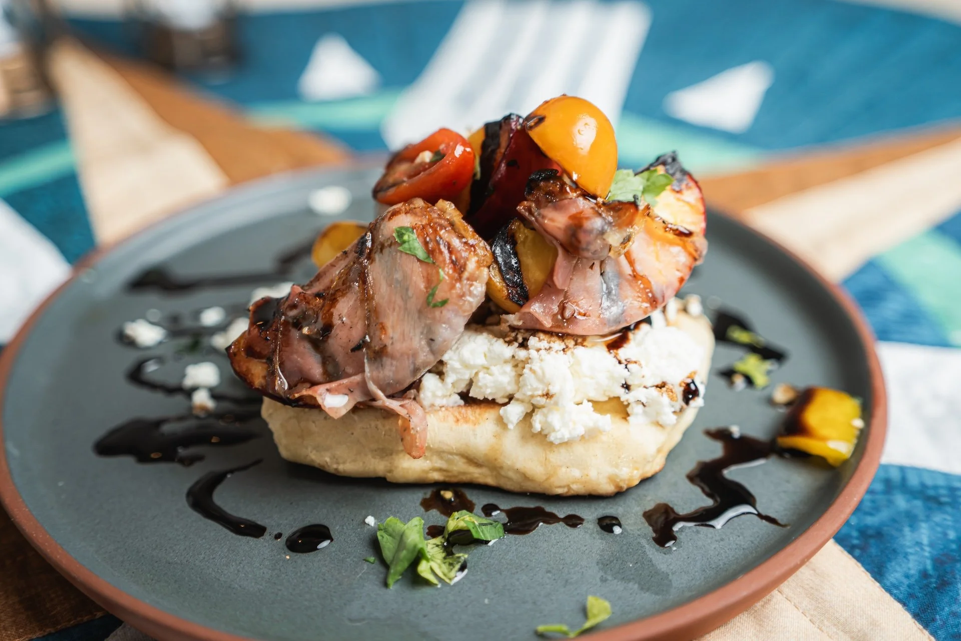 An open-faced sandwich with grilled vegetables and meat, garnished with fresh herbs and drizzled with balsamic glaze, served on a grey plate. Food Photographer in Kalispell, Montana in the Flathead Valley