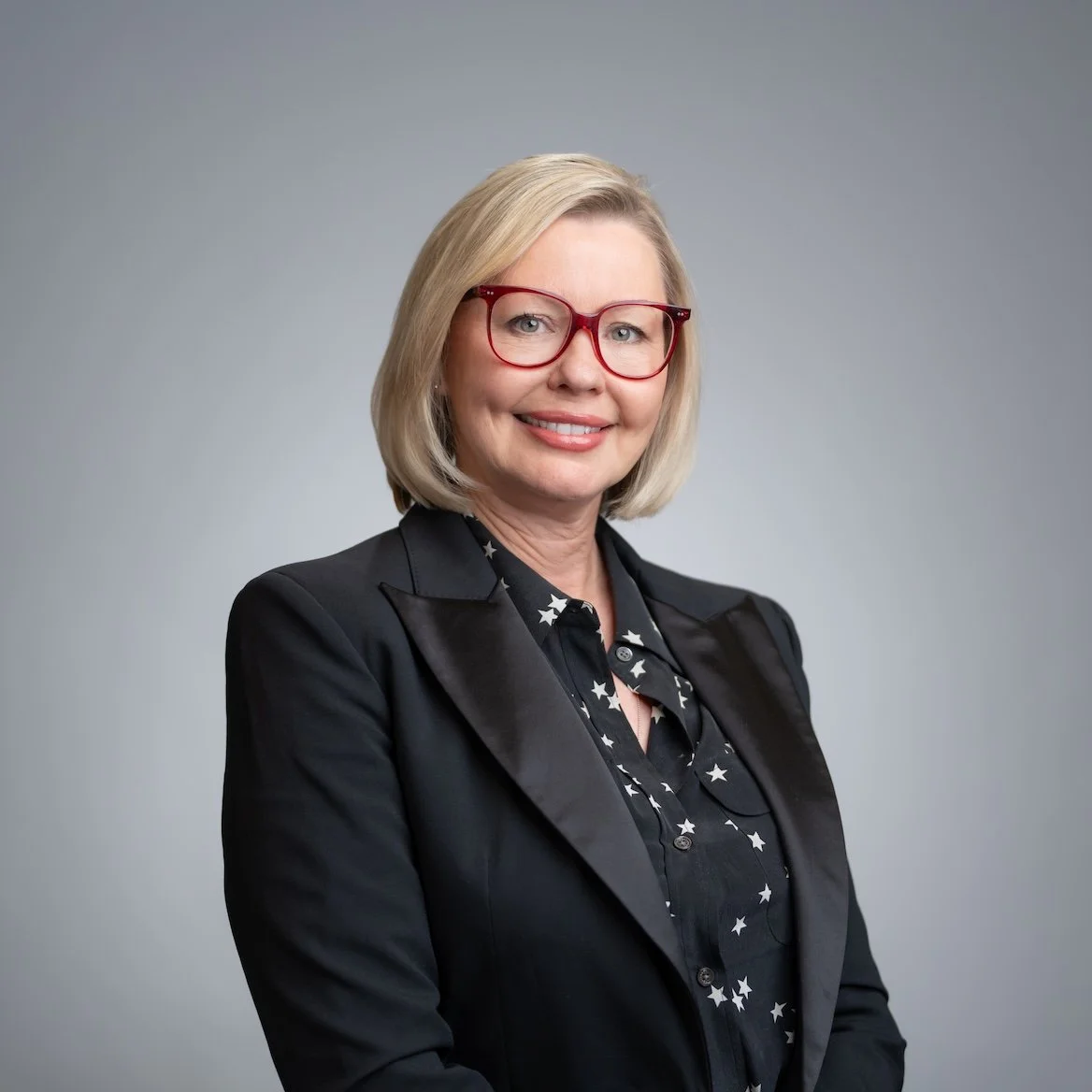 Woman with blonde hair wearing red glasses, black blazer, and star-patterned shirt. Professional Headshot and Portrait Photographer in Kalispell, Montana in the Flathead Valley.