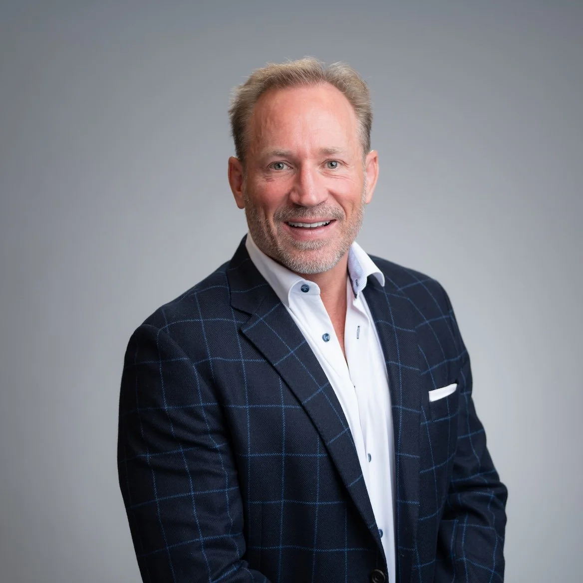 Smiling man in a suit with a checked pattern against a gray background. Professional Headshot and Portrait Photographer in Kalispell, Montana in the Flathead Valley.
