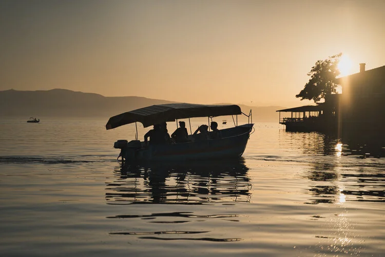 Silhouette of a canopy boat on a lake during sunset with mountains and trees in the background.