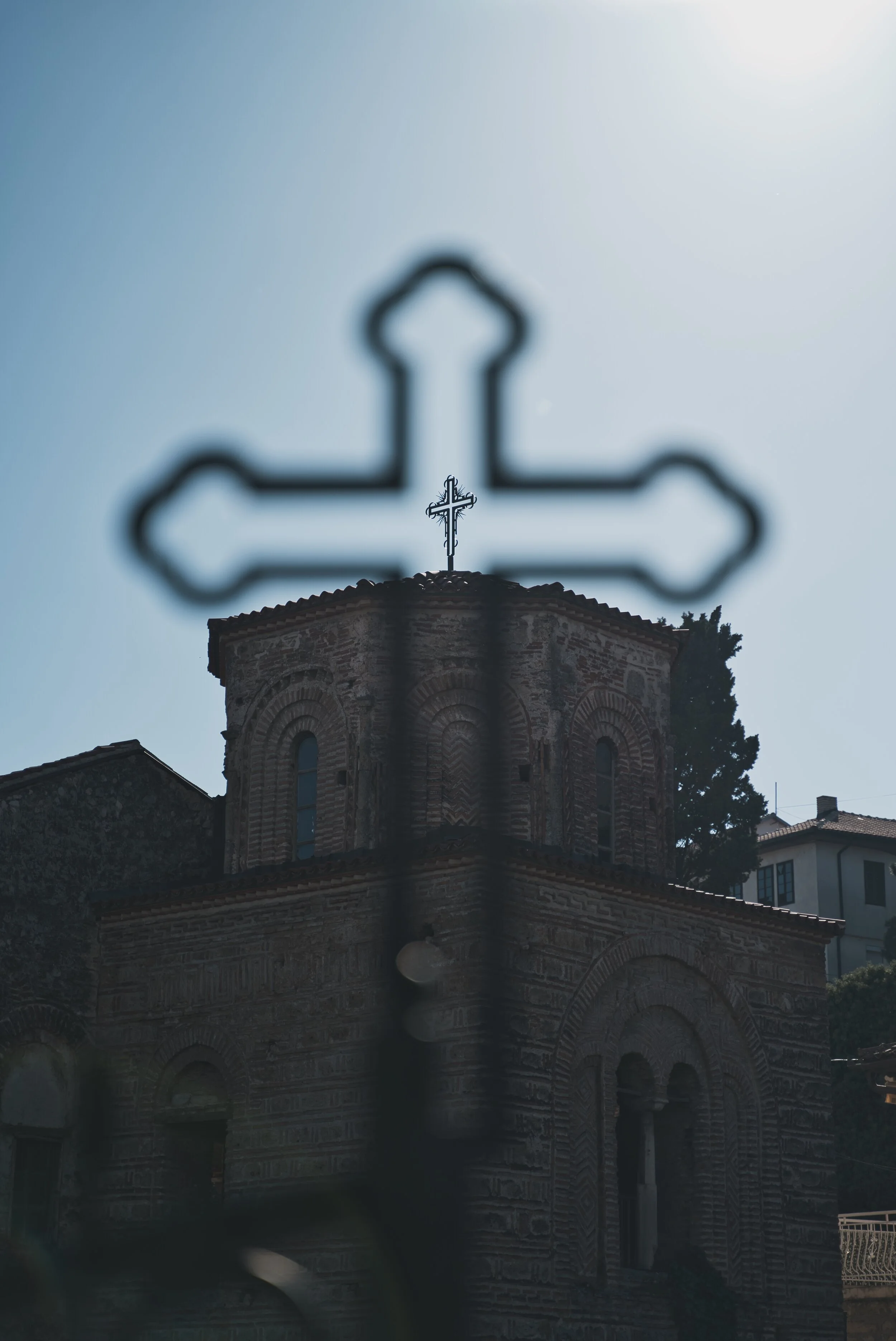 Silhouette of a cross on a church building against a clear blue sky, with the building partially obscured by an out-of-focus foreground cross shape.