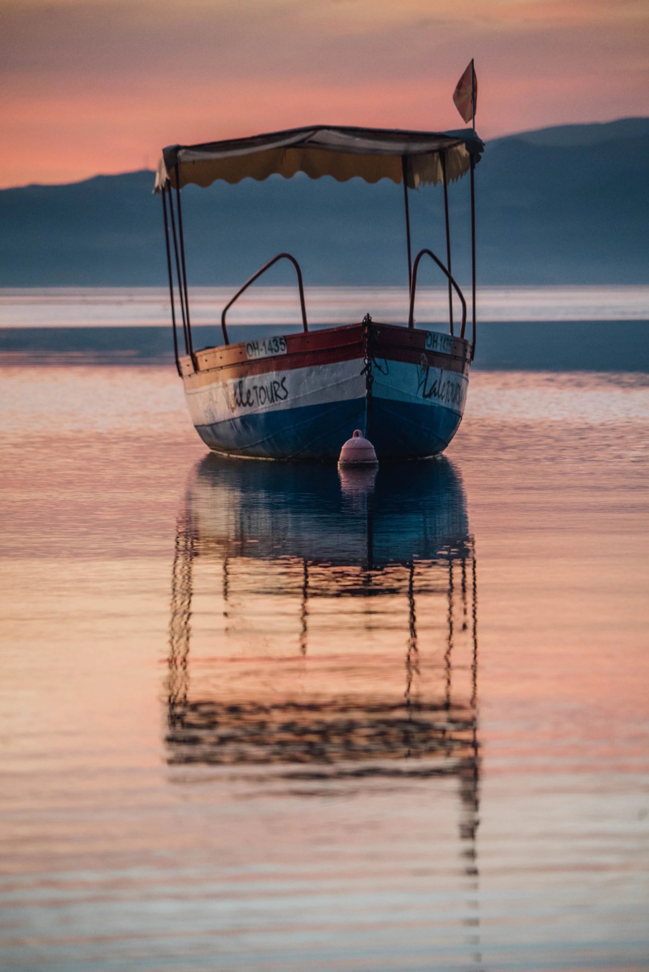 Boat on calm water during sunset, with mountains in the background.
