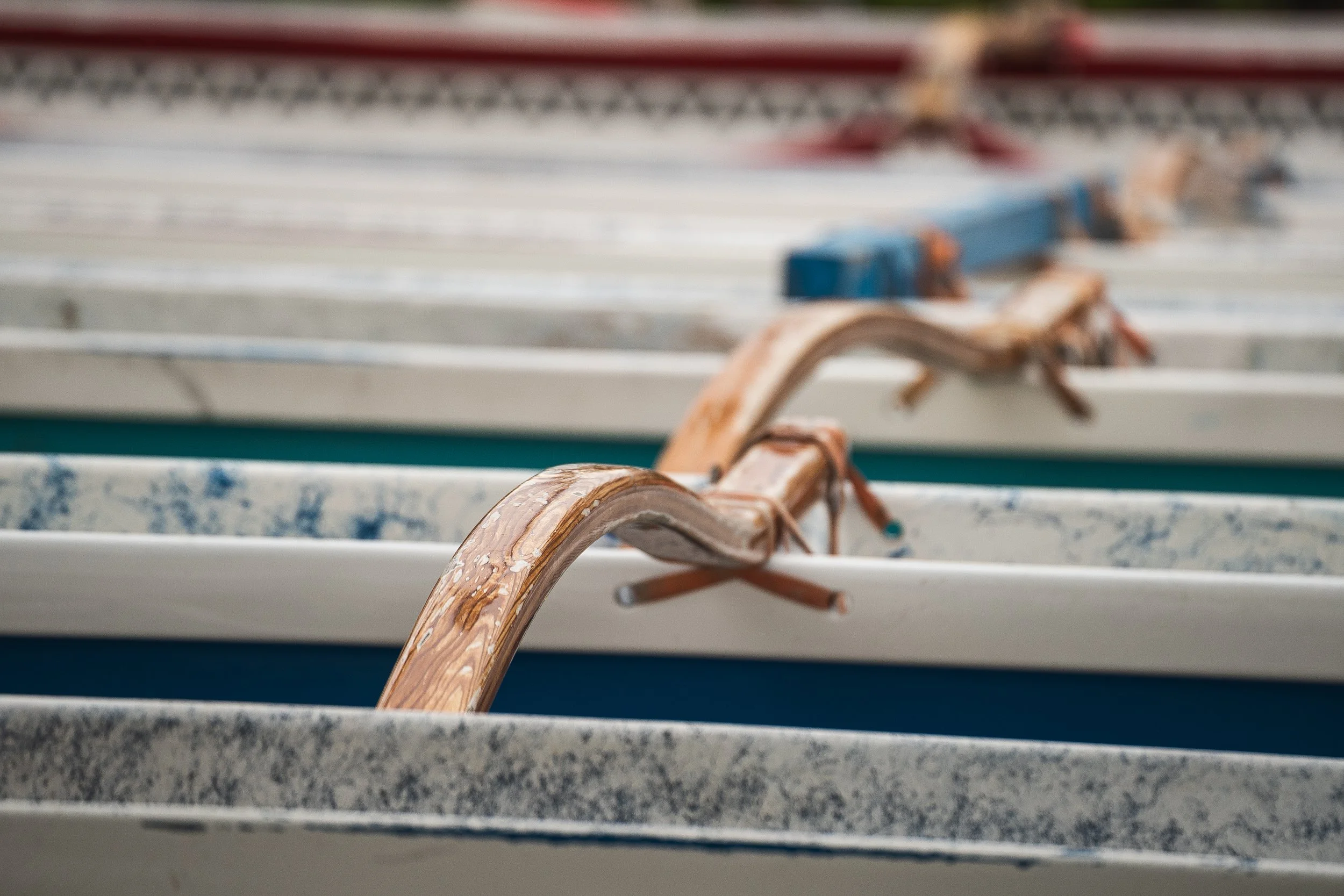 Close-up of a wooden lounge chair with curved handle in front of other similar chairs, showing weathered wood and chipped paint.