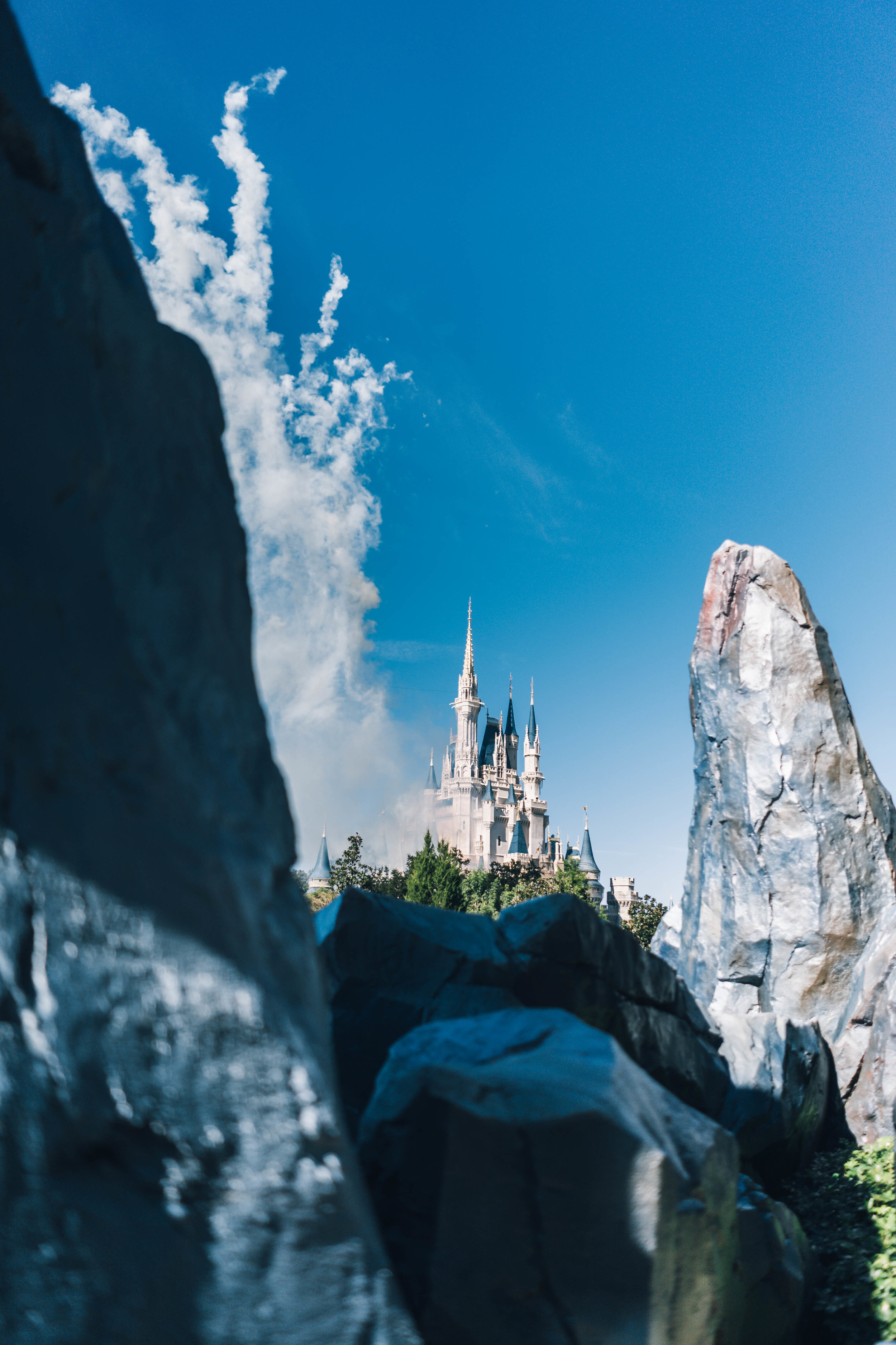 Castle viewed through large rocks and clouds under a blue sky.