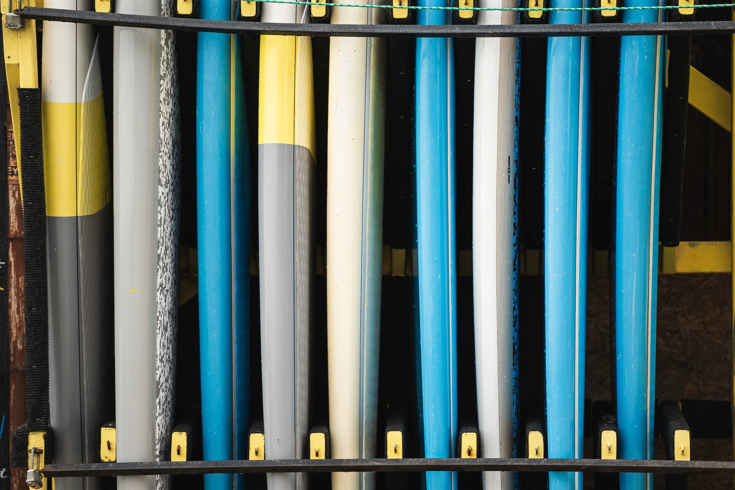 A rack of colorful surfboards stored vertically, featuring yellow, white, blue, gray, and black designs.