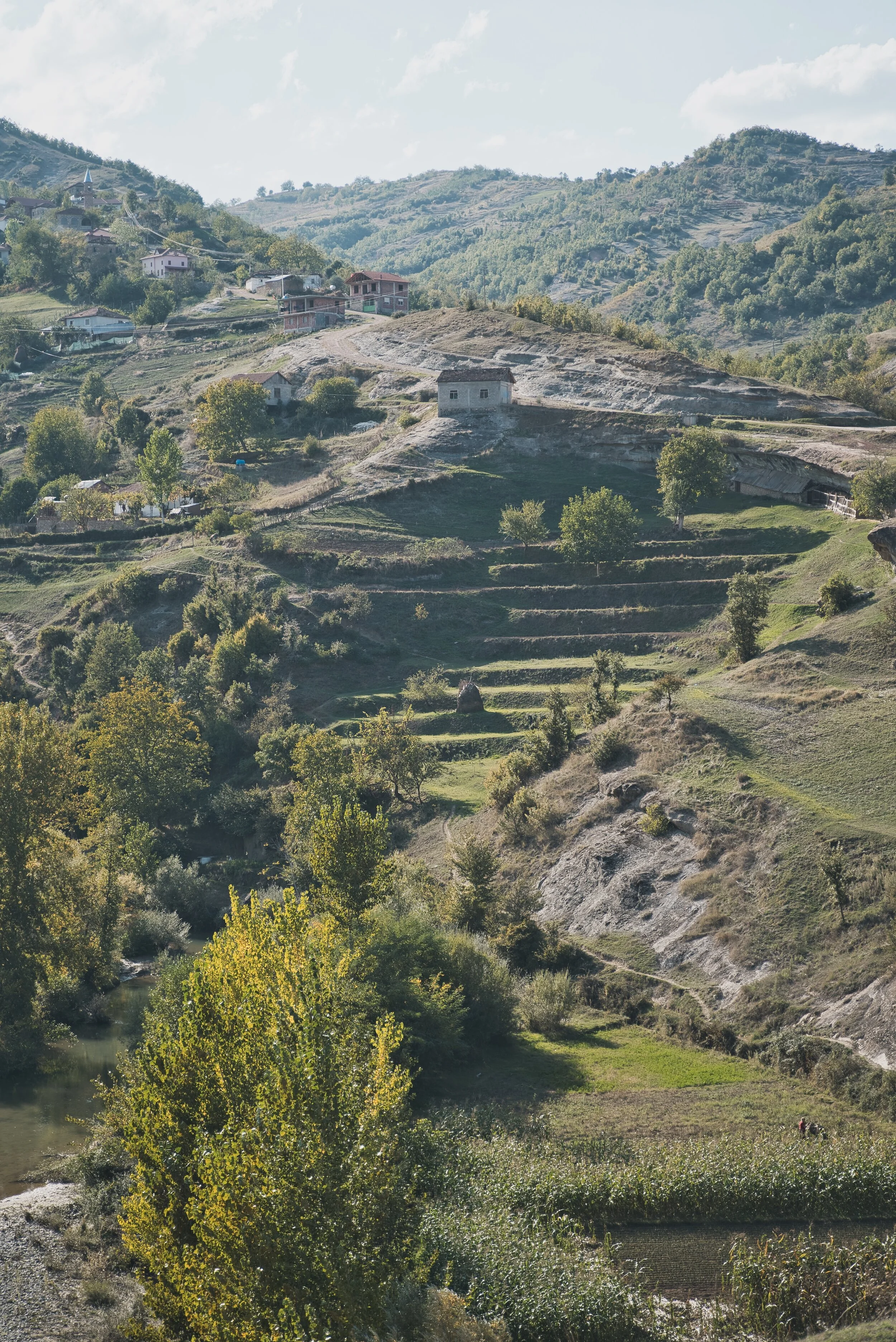 Hilly landscape with terraced fields, scattered trees, and several houses on slopes.