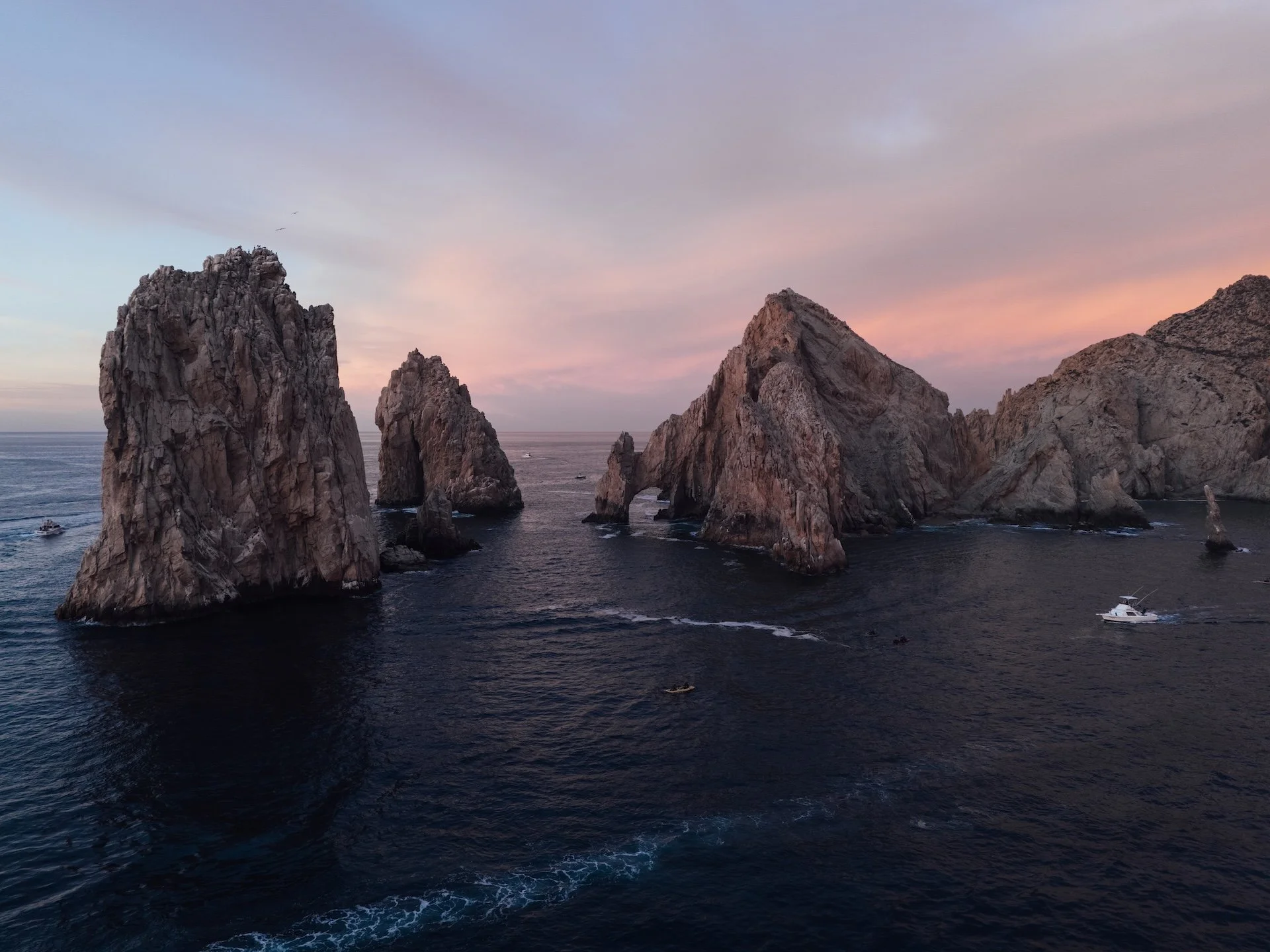 Sea stacks and rocky formations in the ocean at sunset with boats around.