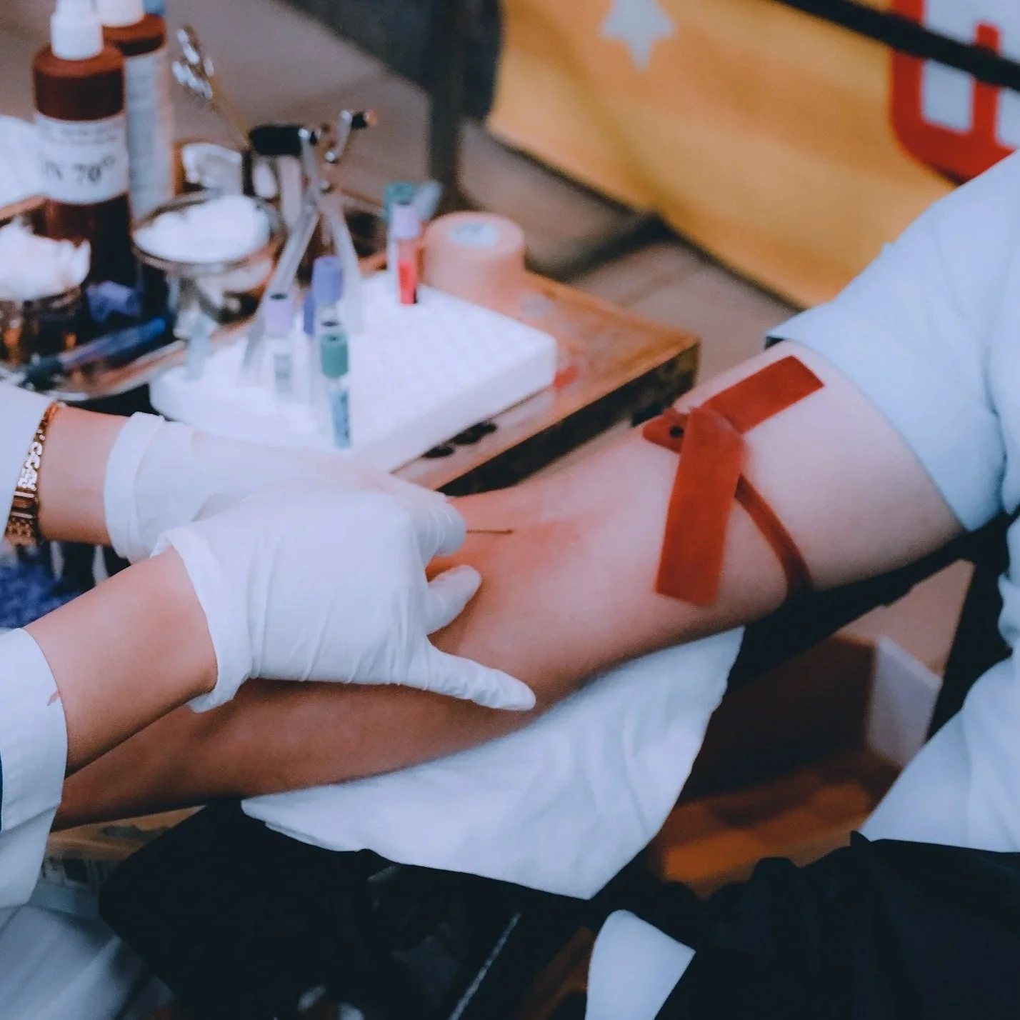 A person donating blood, with a medical professional preparing to draw blood from their arm. The person's arm has a bandage on it, and medical supplies are visible on a nearby table.