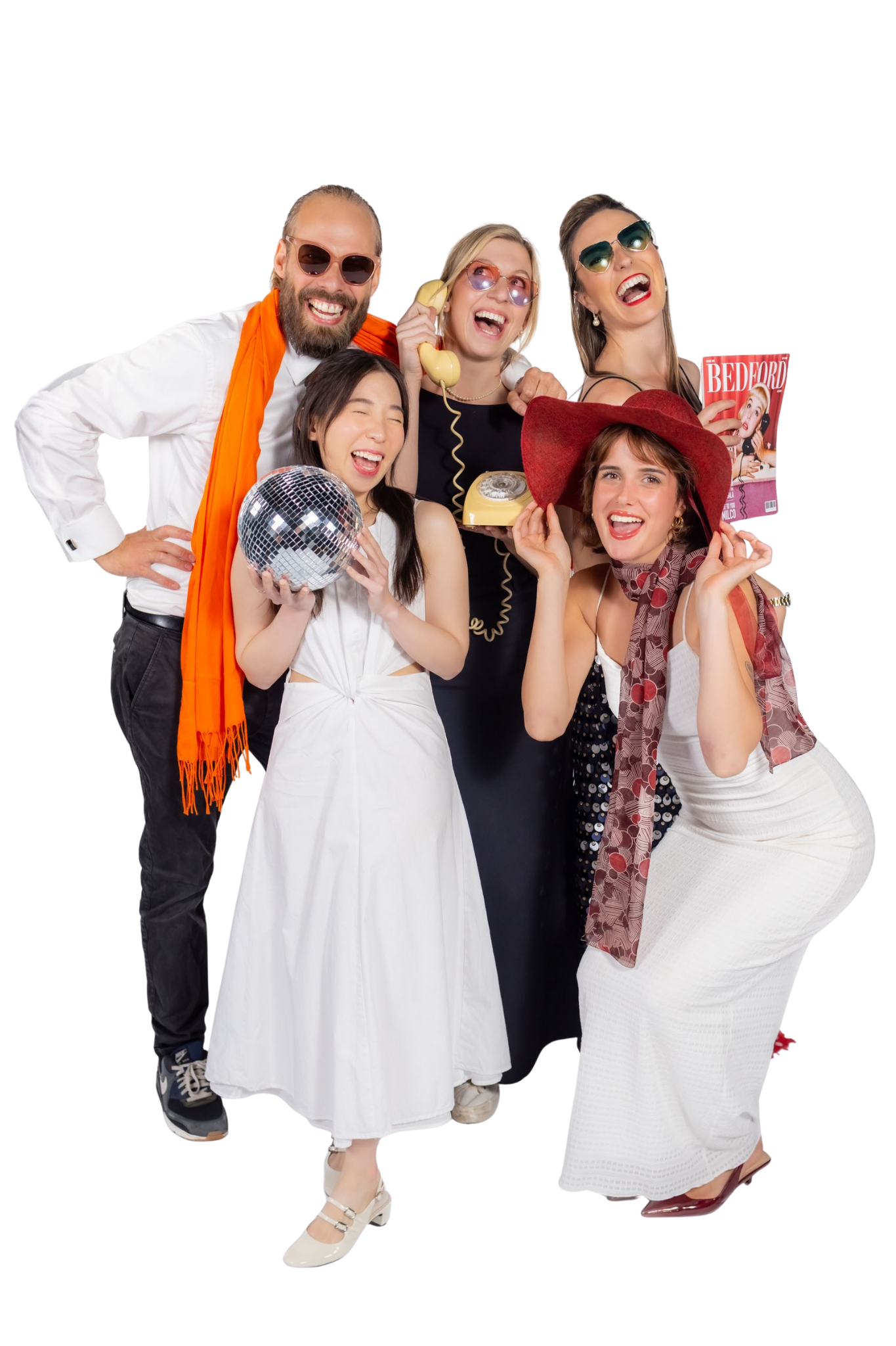 Group of five friends dressed in retro style, celebrating with props like a disco ball, a big red hat, a yellow rotary phone, sunglasses, and a magazine.