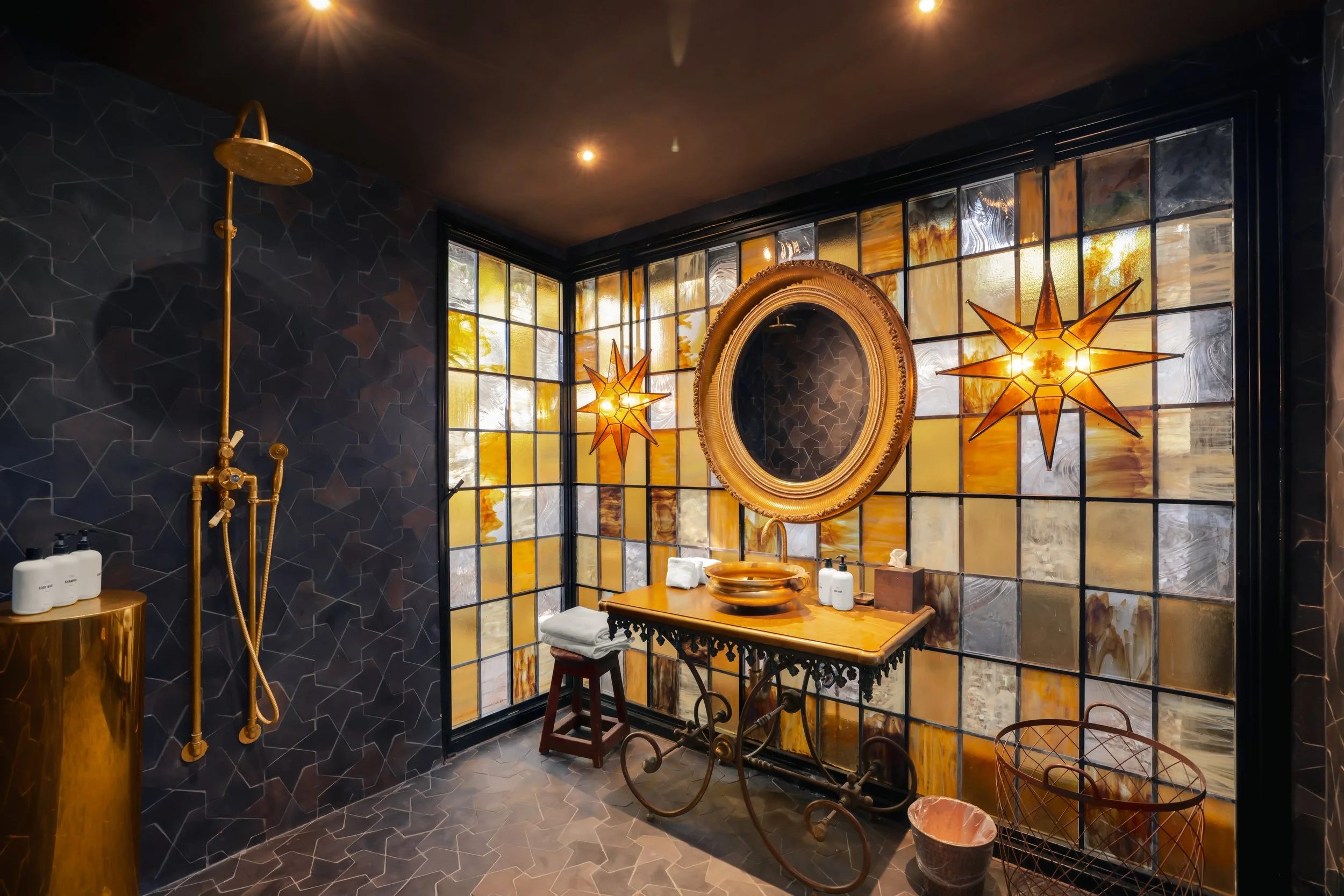 Luxurious bathroom with dark walls, golden fixtures, a decorative mirror, a backsplash of stained glass, and star-shaped pendant lights.