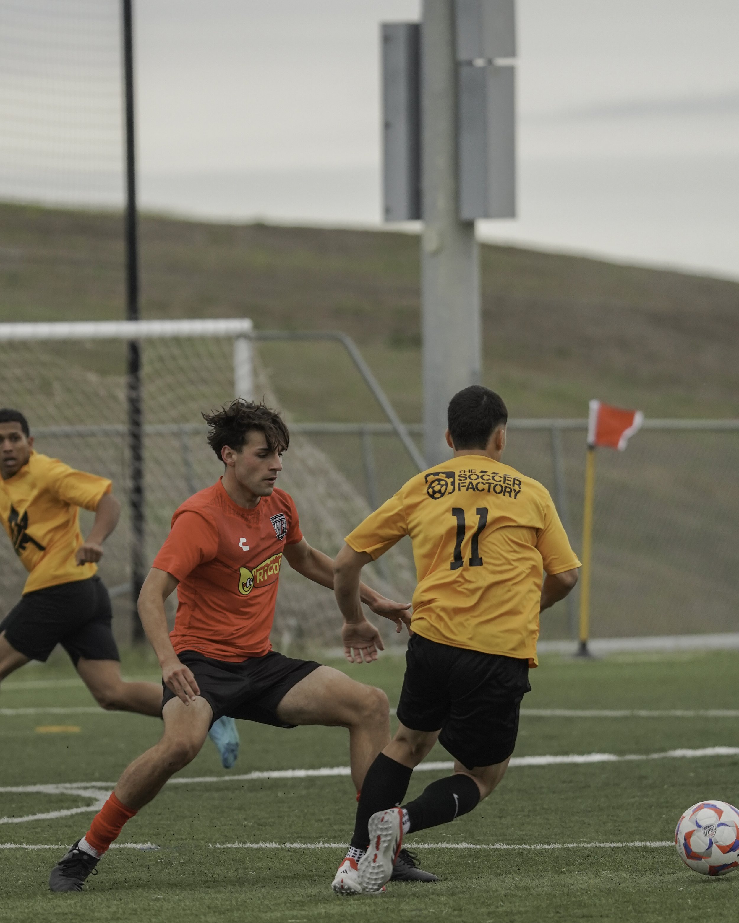 Youth soccer game on a green field with players in red and yellow jerseys, one in red with the number 5, one in yellow with the number 11, actively competing for the ball near the sideline.