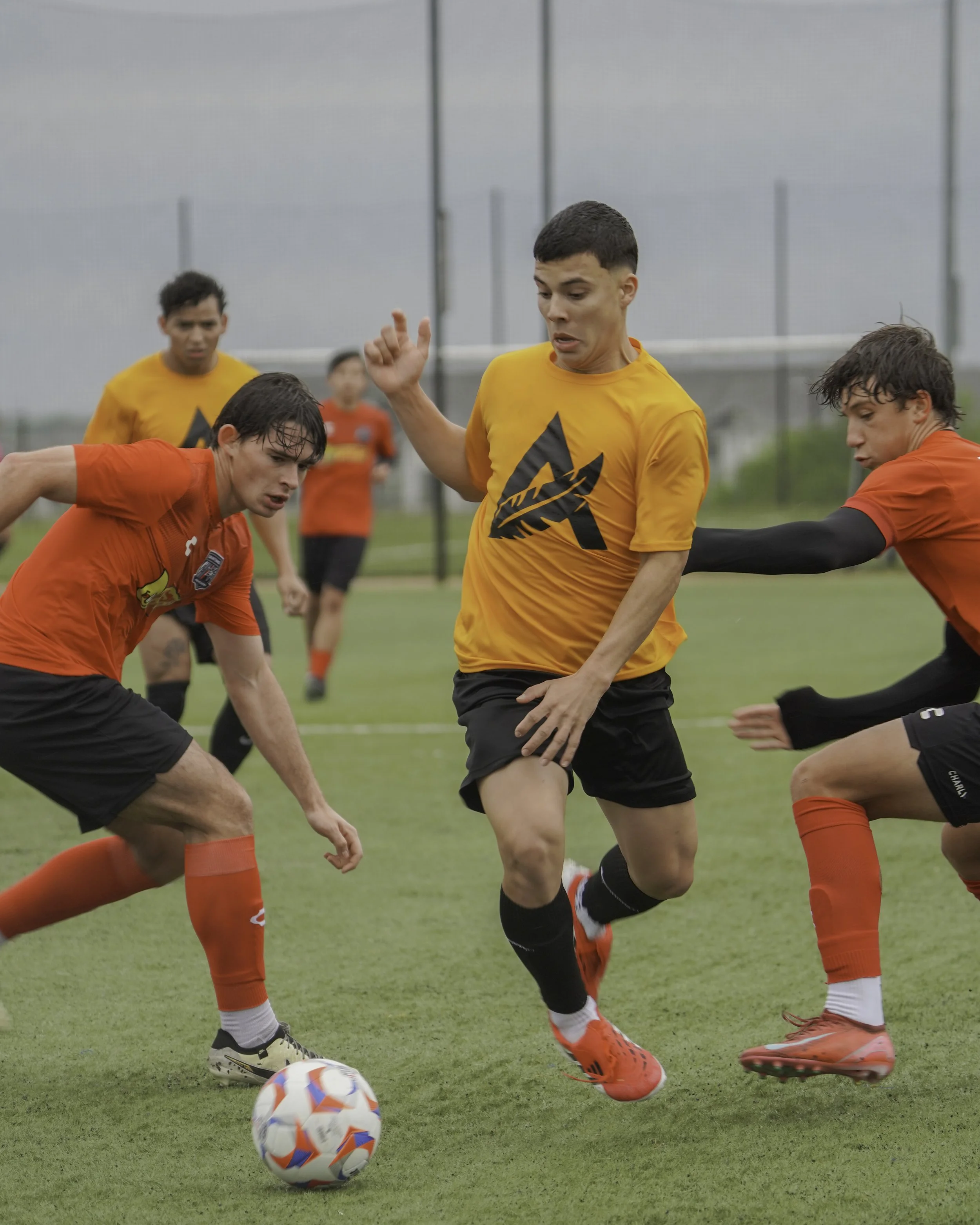 Soccer players competing for the ball on the field during a game, with players wearing orange and red jerseys.