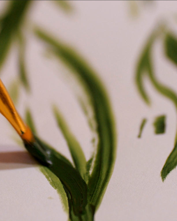 Close-up of a paintbrush applying green watercolor paint on paper with green brushstrokes.