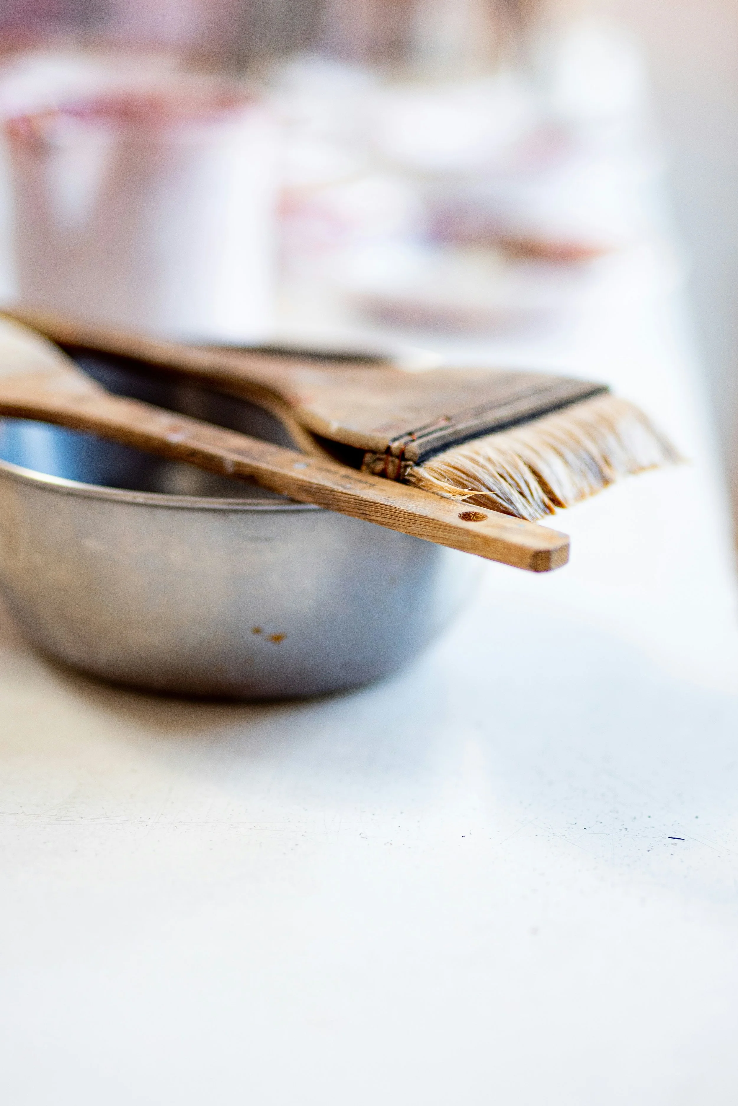 Close-up of a kitchen countertop with a metal mixing bowl, a wooden spatula, and a small brush resting on the bowl.