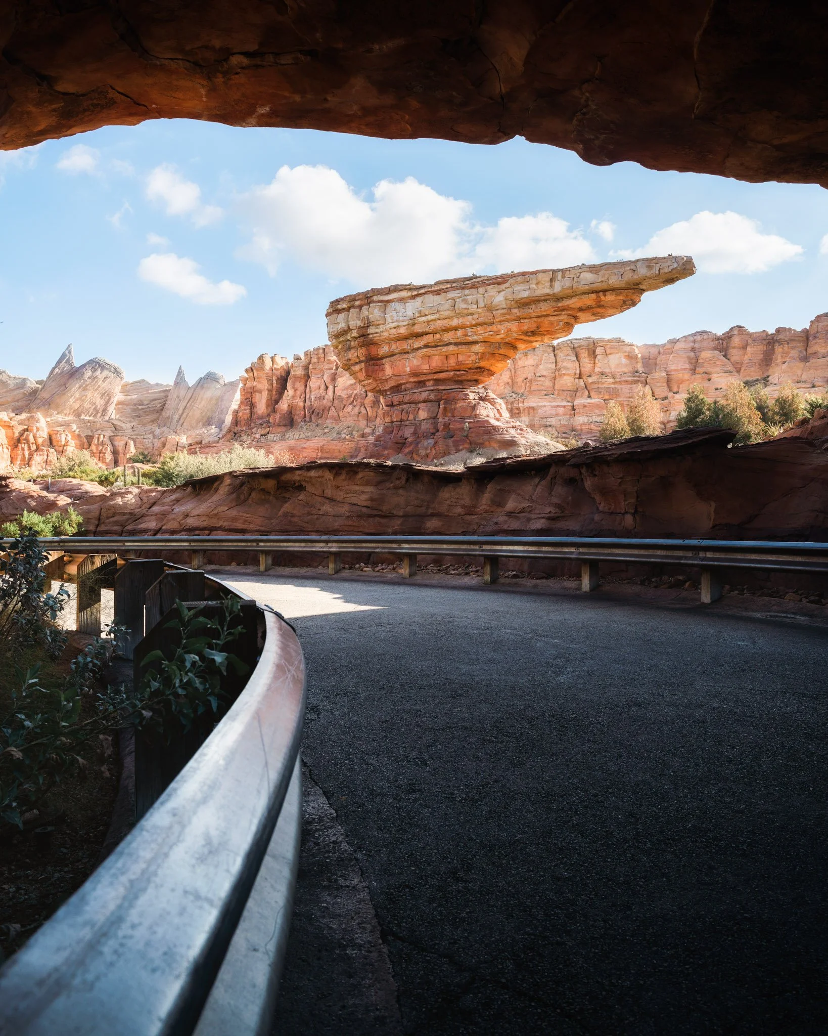 View from inside a rock tunnel looking out over a desert landscape with red rock formations and blue sky.