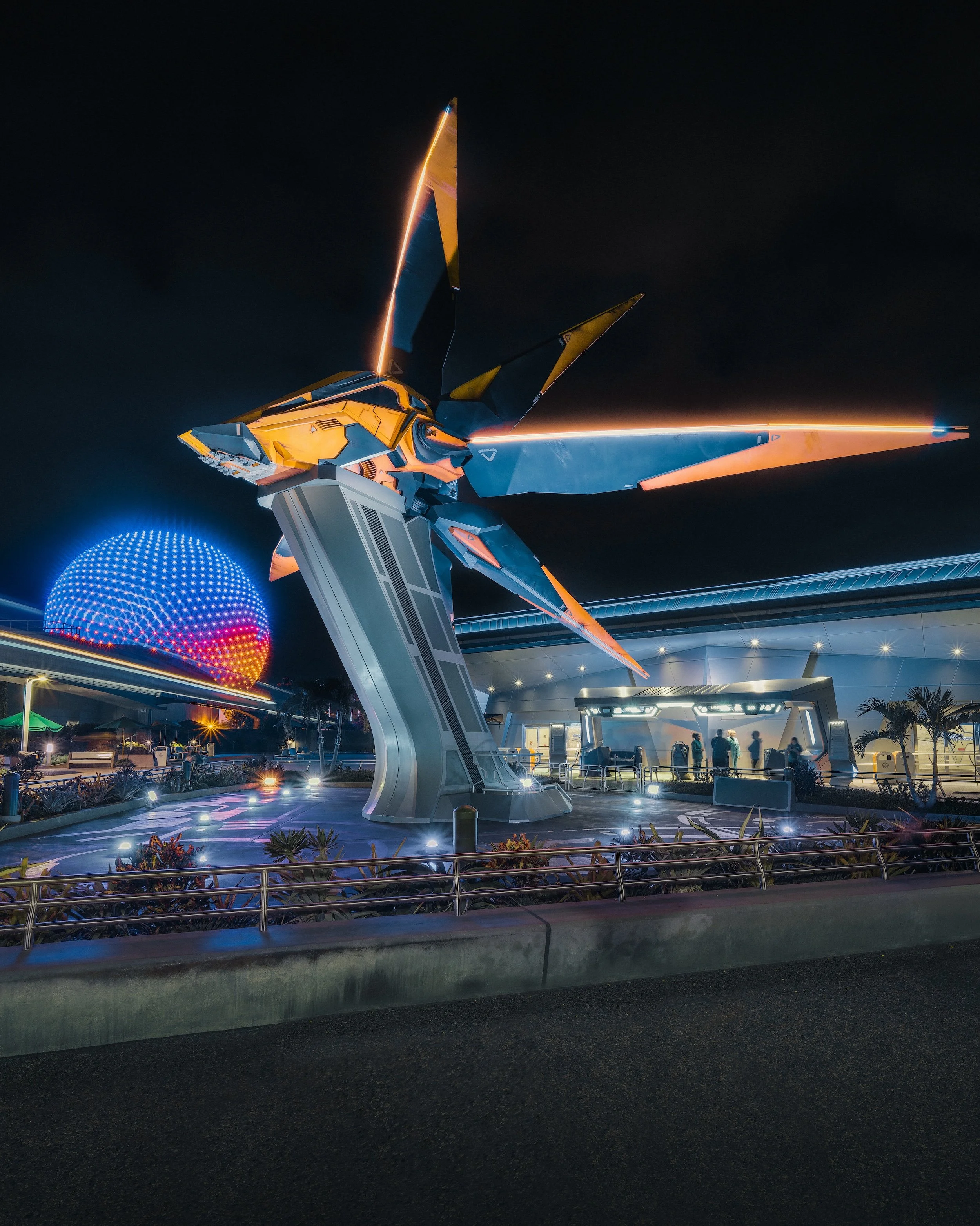 A futuristic sculpture of a robot or mechanical creature with sharp, angular features, illuminated at night, with colorful lights and a world map in the background.