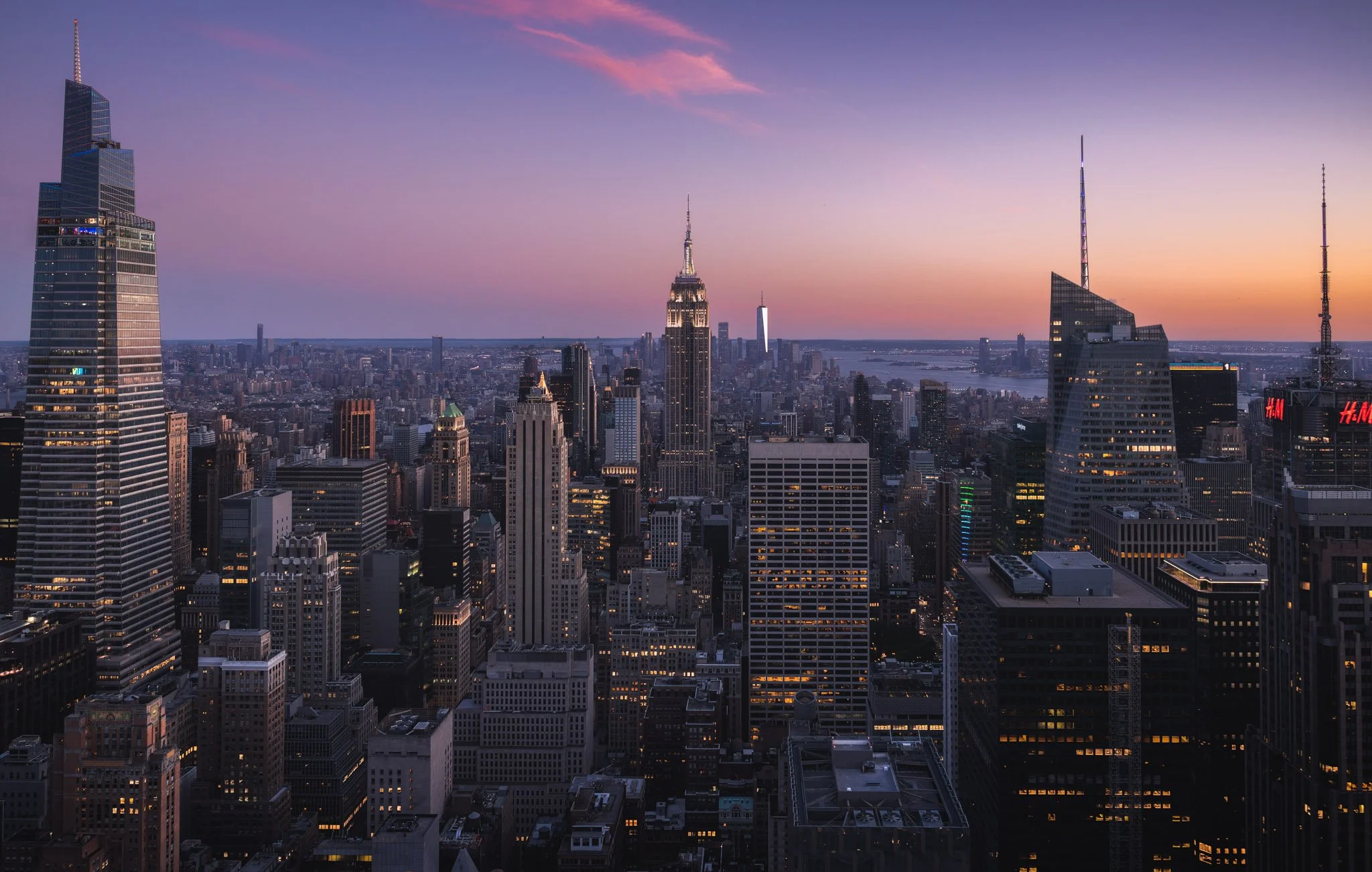 Skyline of New York City at sunset with tall buildings including the Empire State Building and other skyscrapers.