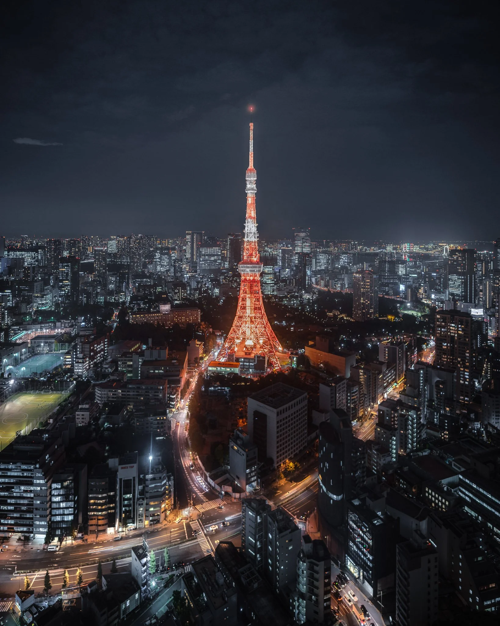 Nighttime cityscape with illuminated skyscrapers and Tokyo Tower lit in orange and white, seen from a high vantage point.