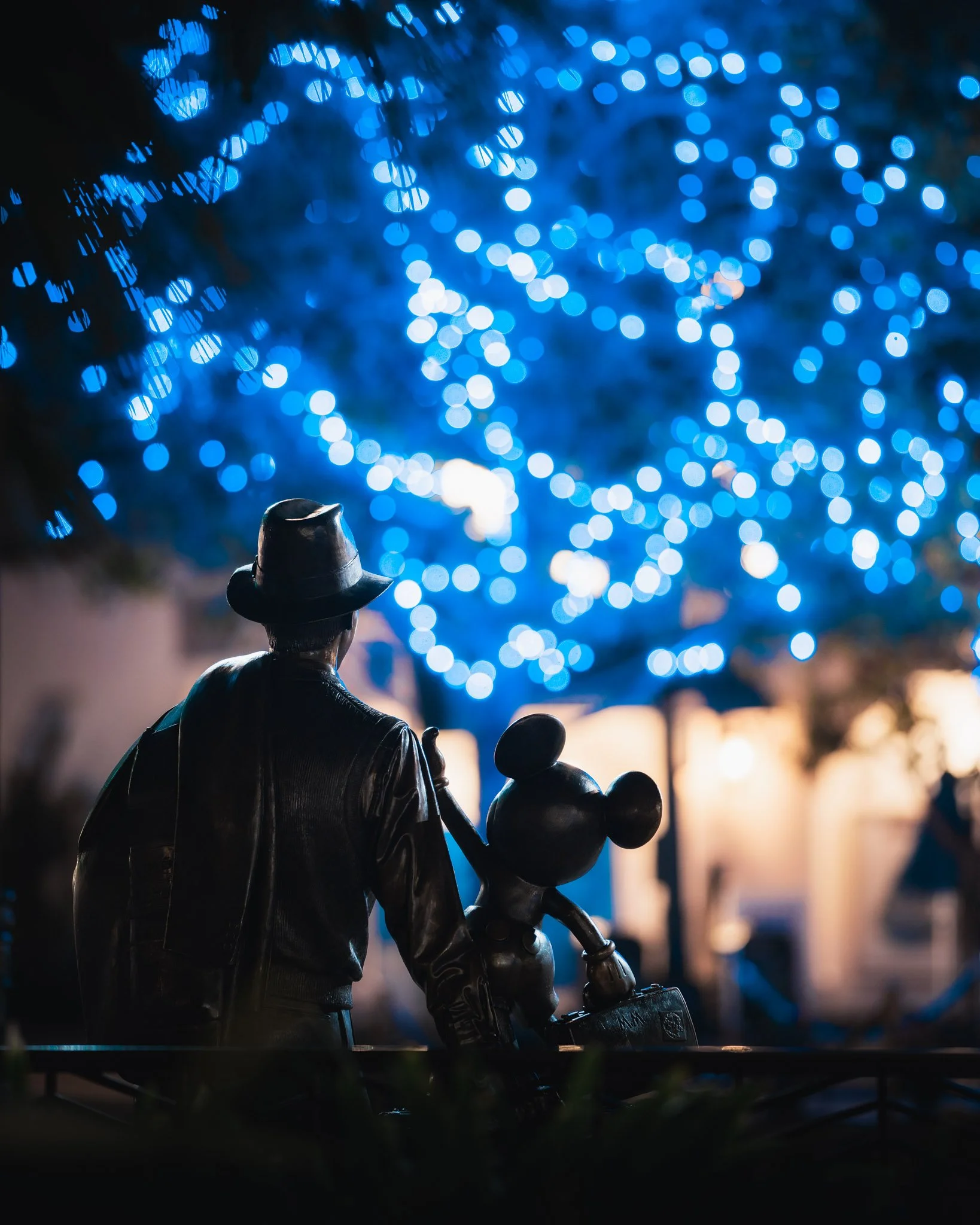 Statue of a man holding a child, with a background of blue Christmas lights in a bokeh effect.