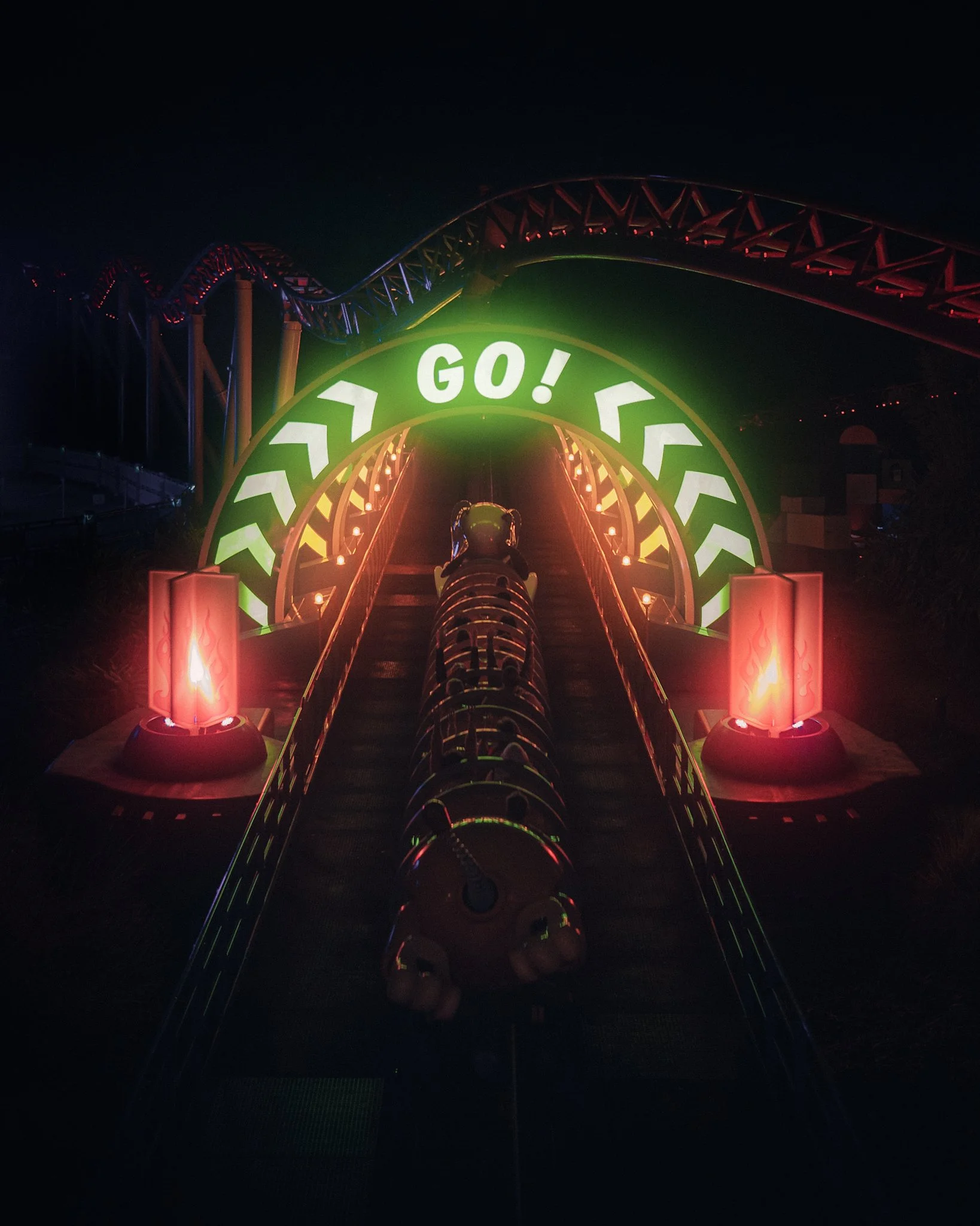 Nighttime amusement park ride with illuminated signage saying 'Let's Go!' and a roller coaster track in the background.