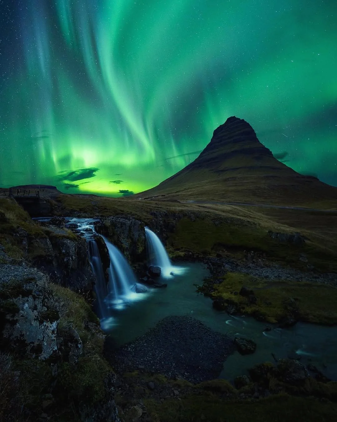 Northern lights illuminating the night sky over Kirkjufell mountain with waterfalls in the foreground.