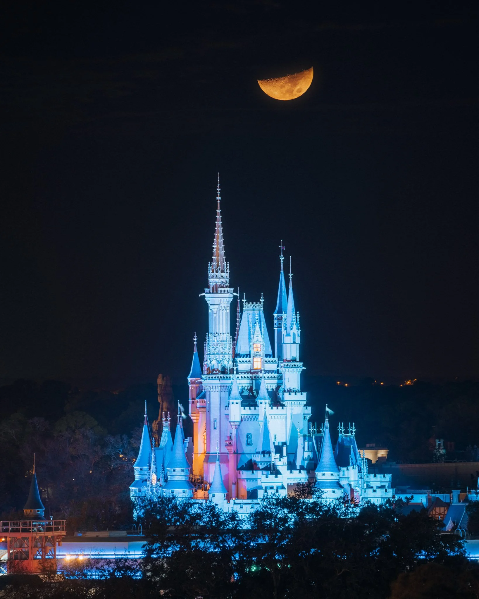 Illuminated Disney castle at night with a waxing gibbous moon in the dark sky