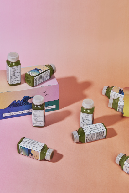 Assorted small green juice bottles on a peach and pink gradient background with a colorful box.