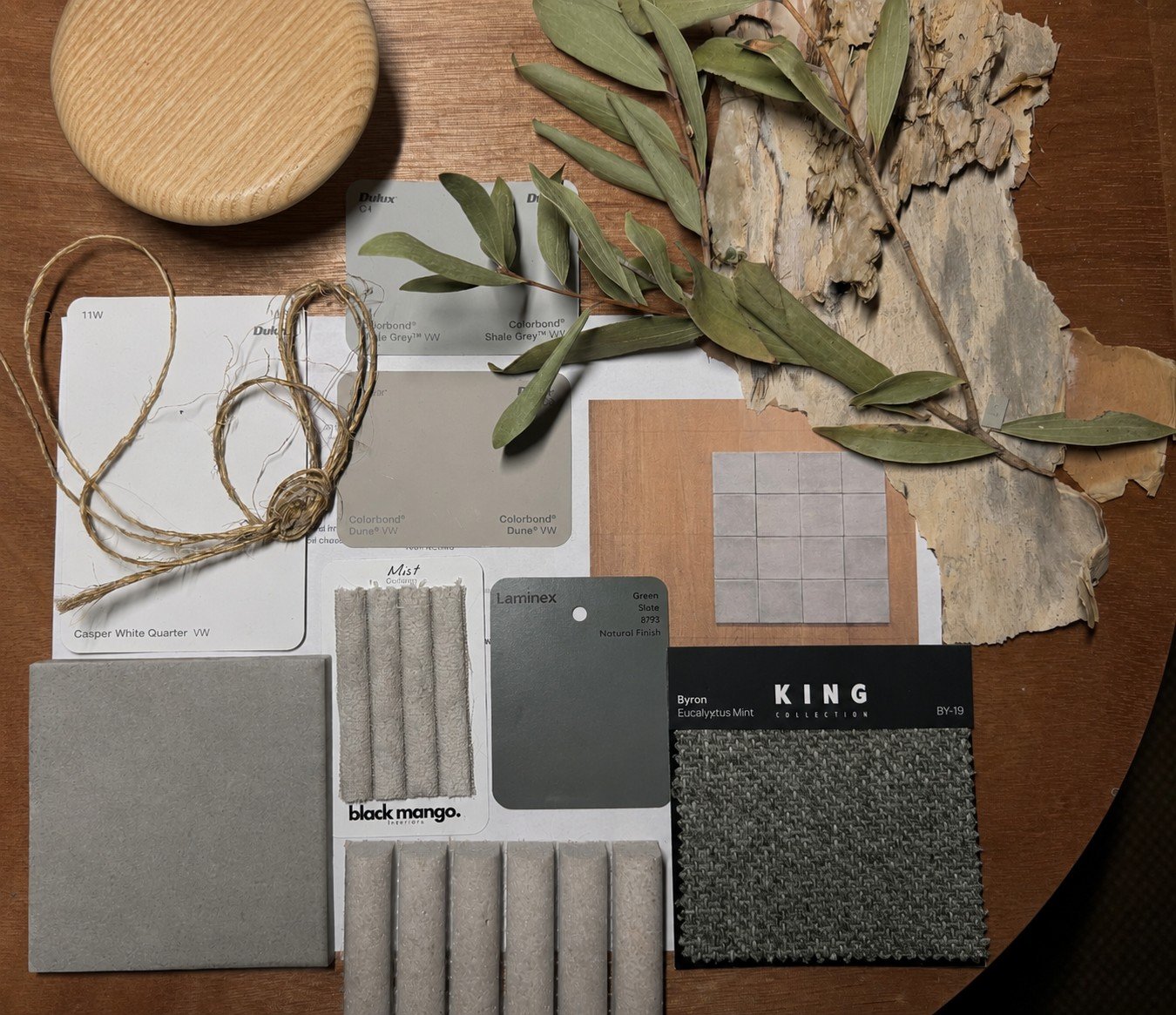 A selection of interior design and decor samples including fabric swatches, paint color samples, natural moss and dried leaves, and a piece of textured tile arranged on a wooden surface.